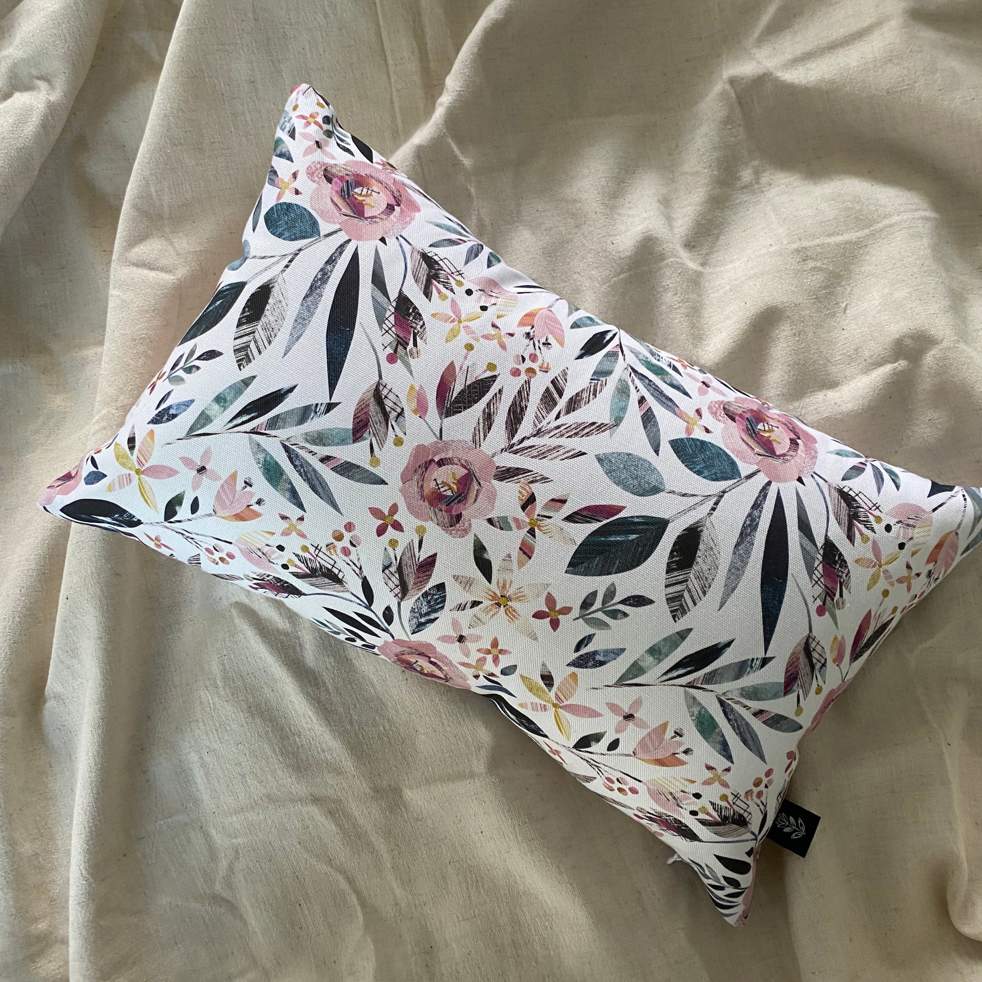 Rectangular Summer Floral Cushion has been laid onto a natural bed sheet.  The print features Pink Roses with Green leaves.