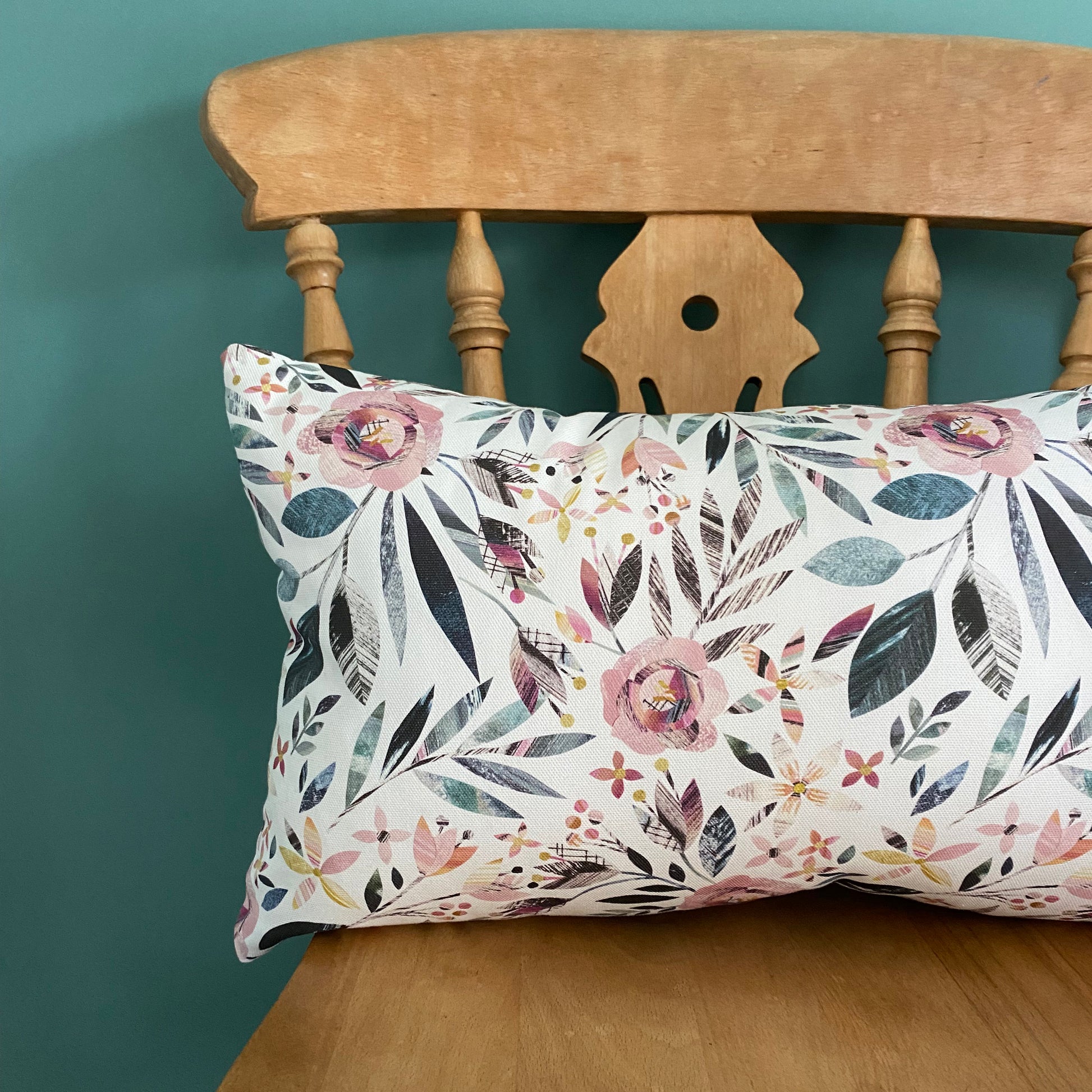 Rectangular Summer Floral Cushion, has been placed on a wooden chair against a Green Blue Wall.