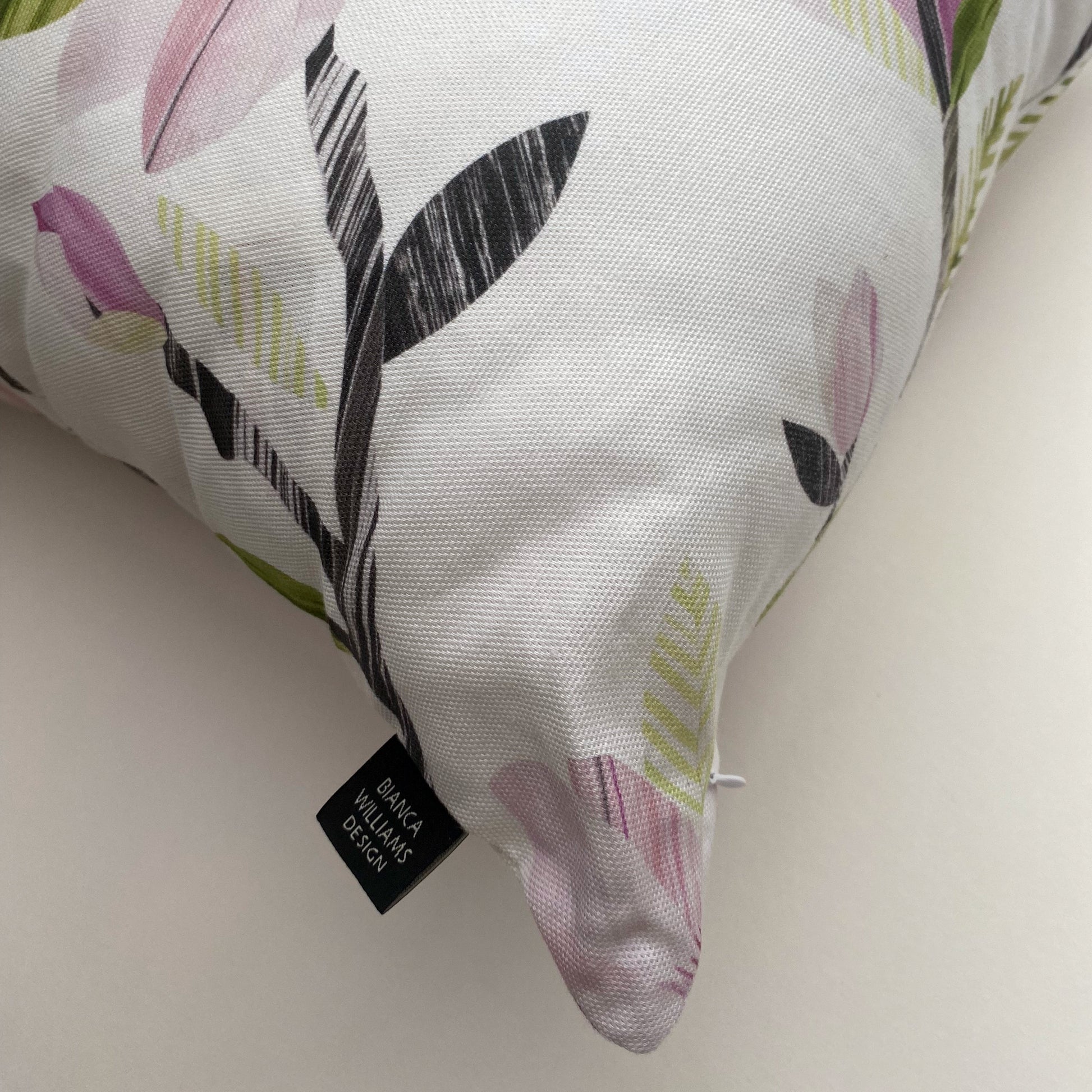 Close up of the corner of a Magnolia cushion, showing the concealed zip and Brand label sewn into the side seams.  The cushion has been placed on a white background.