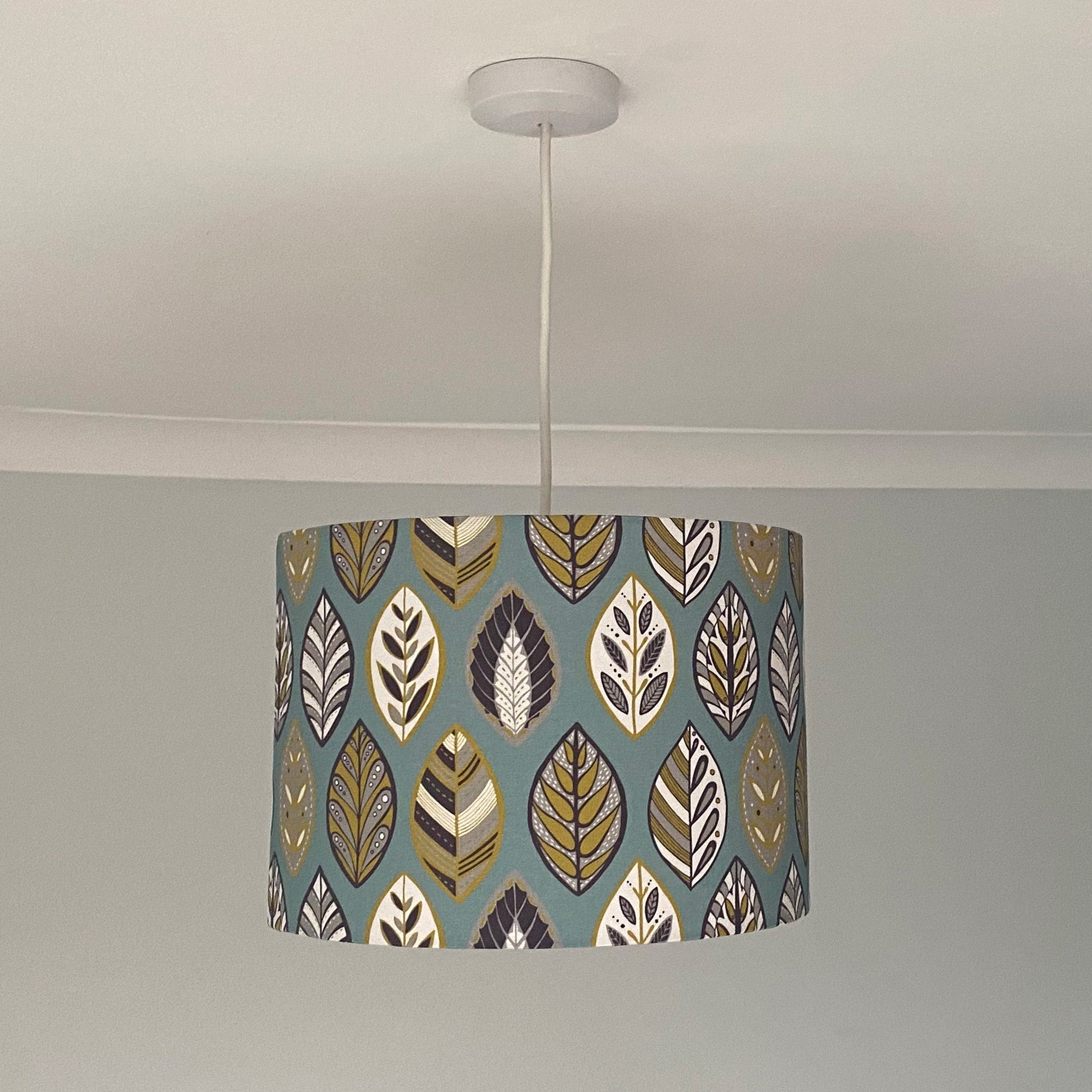 Medium Blue Beech leaf Lampshade, shown here on a ceiling pendant. The pattern features a Skandi style Blue, yellow, grey and white Leaf pattern on a Blue Background.