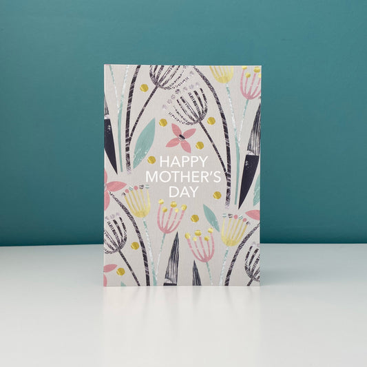 Mother's Day Card featuring textured seed pods in Black, green, yellow and Pink on a pale grey background.  The card says Happy Mother's Day and has been stood on a white shelf with a Blue green Background.