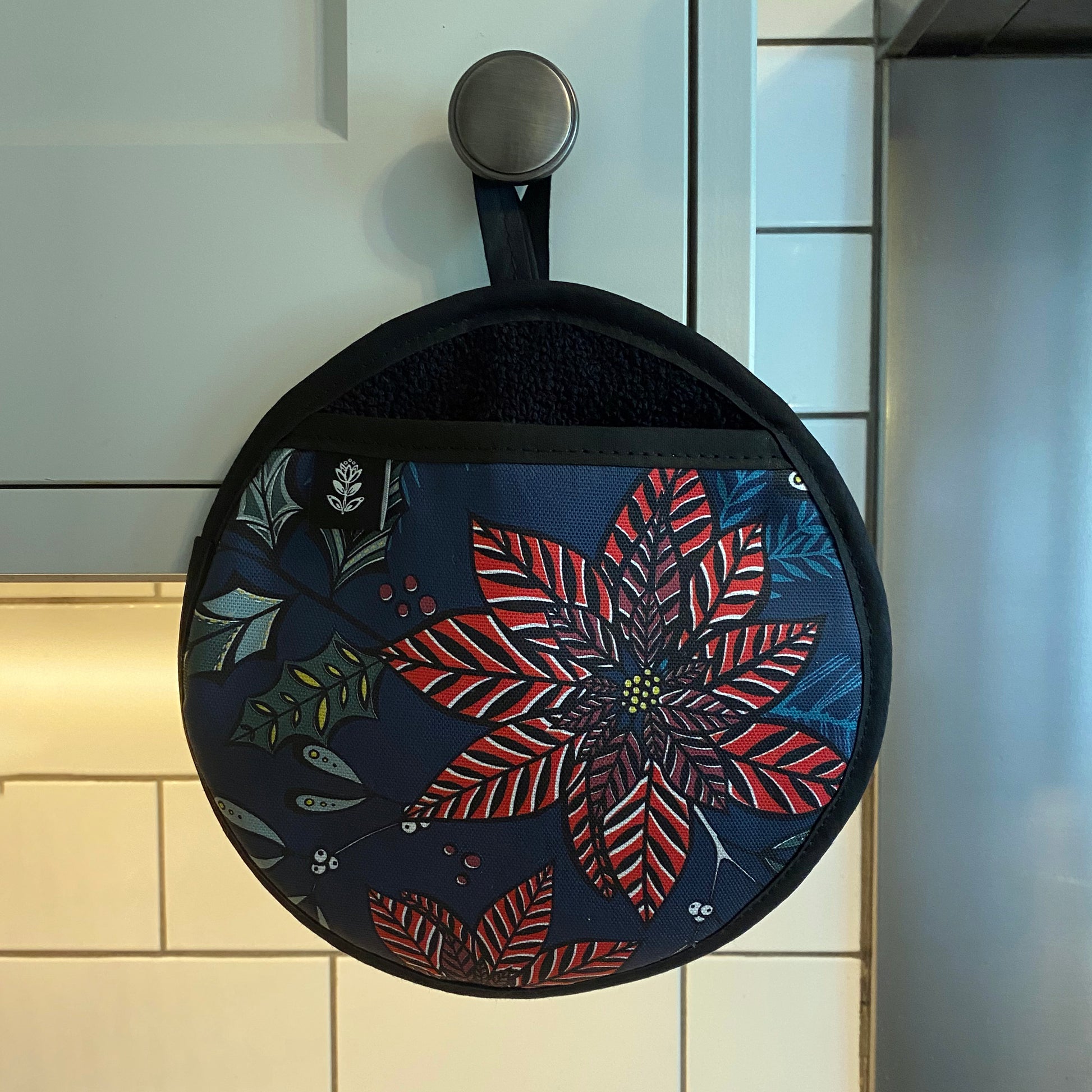Navy Poinsettia pot holder has been hung on a grey kitchen cupboard handle.