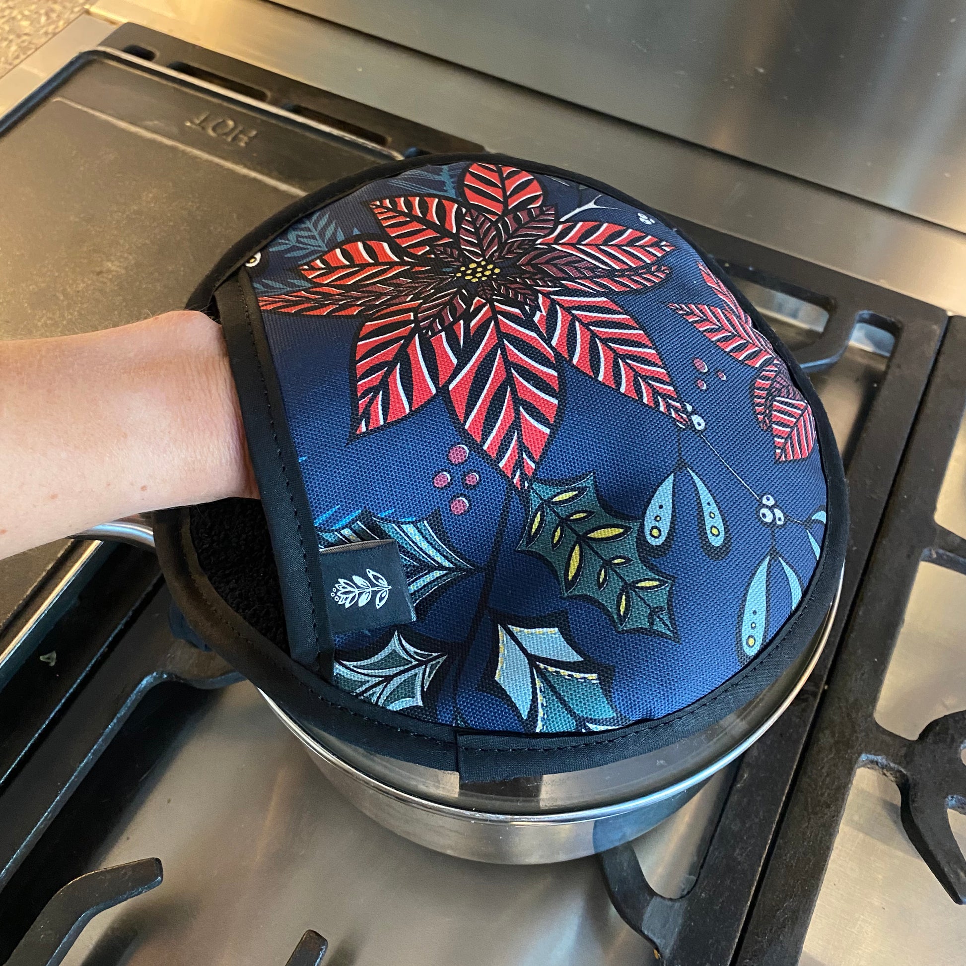 Navy Poinsettia pot grab being used to remove a hot saucepan lid off a saucepan.