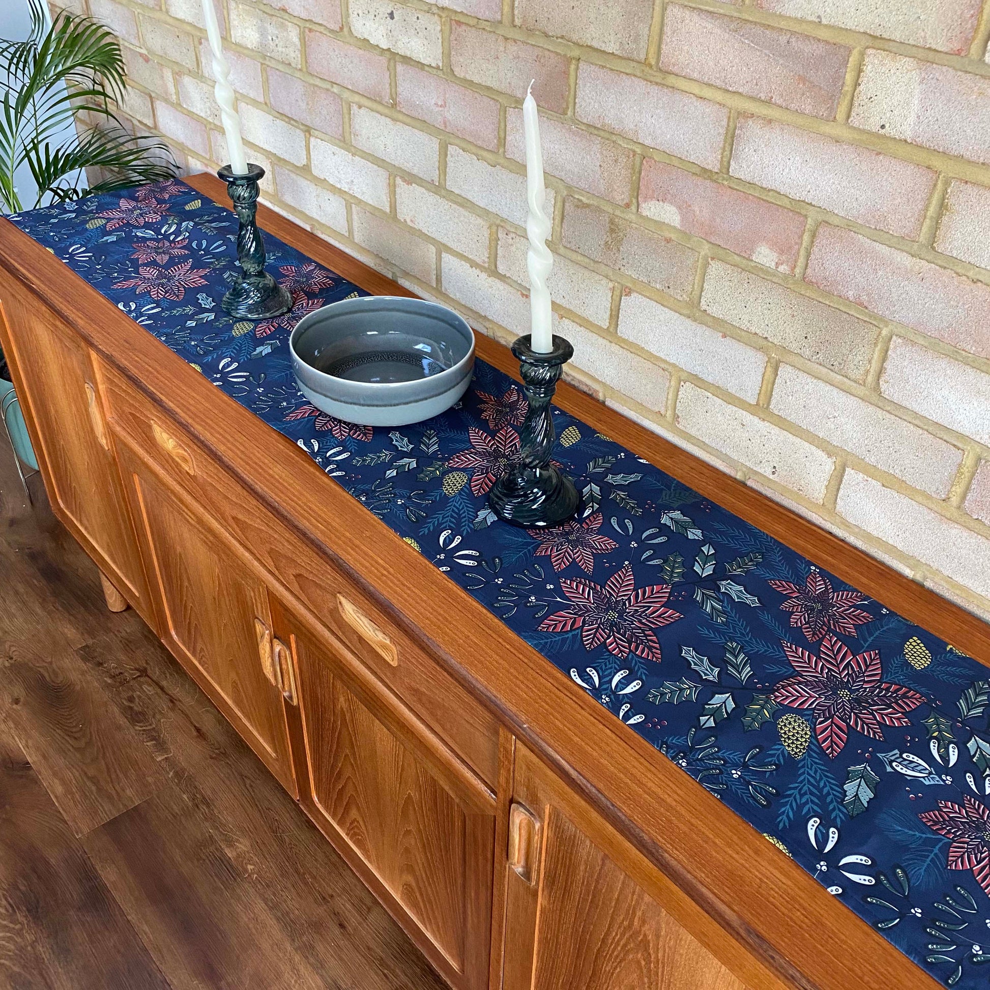 Navy Christmas Table Runner has been placed on a wooden side board.