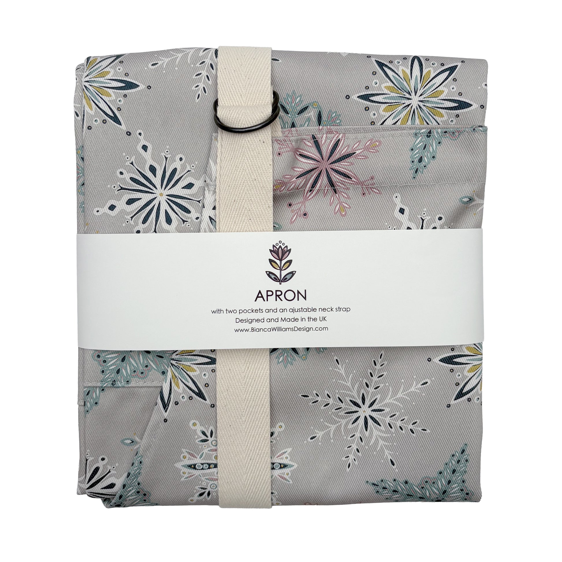 A grey snowflakes apron has been packed in a Bianca Williams Design branded packaging and has been placed on a white background.