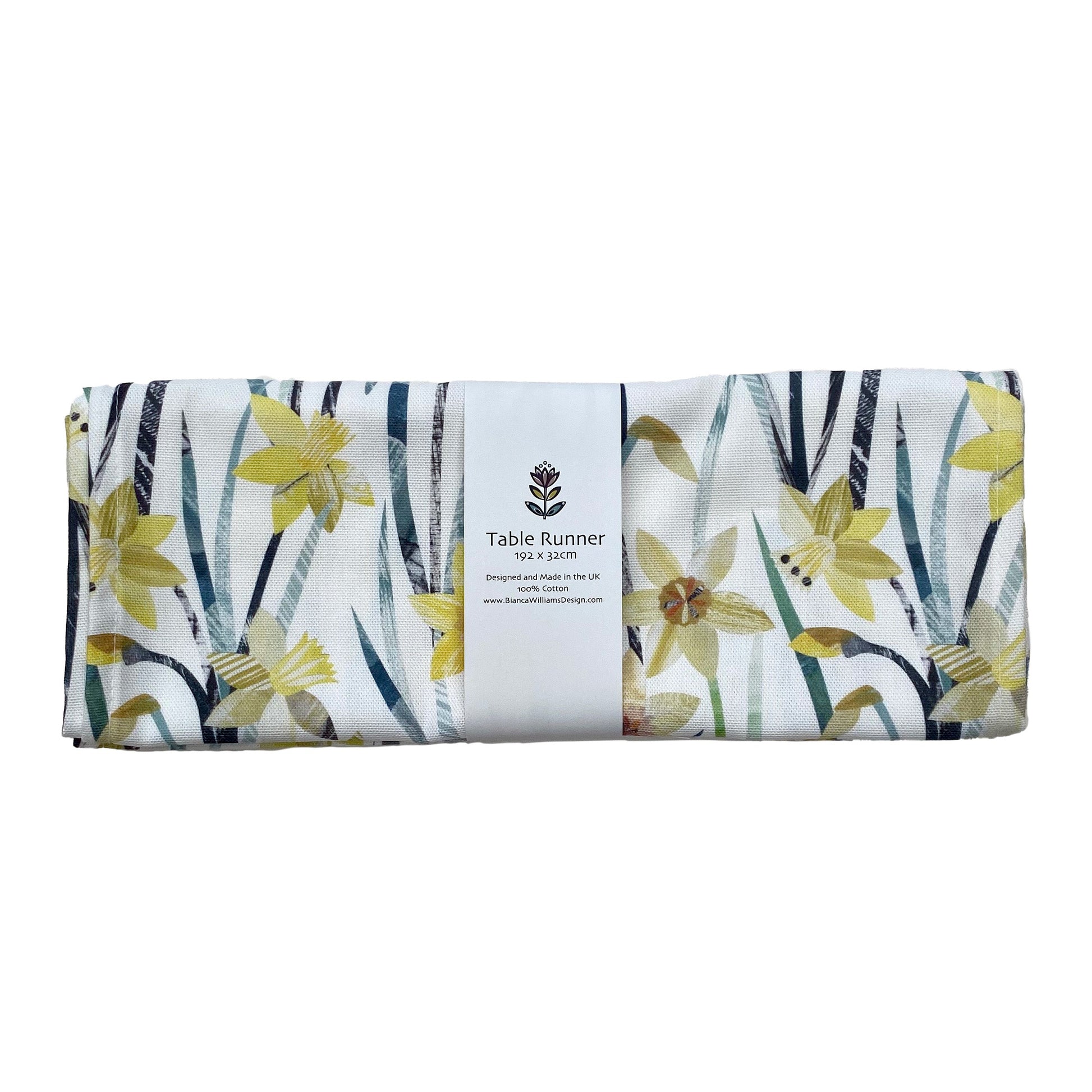 A folded and packaged Daffodil Table Runner, which has been packaged in a branded white belly band and place on a white background.