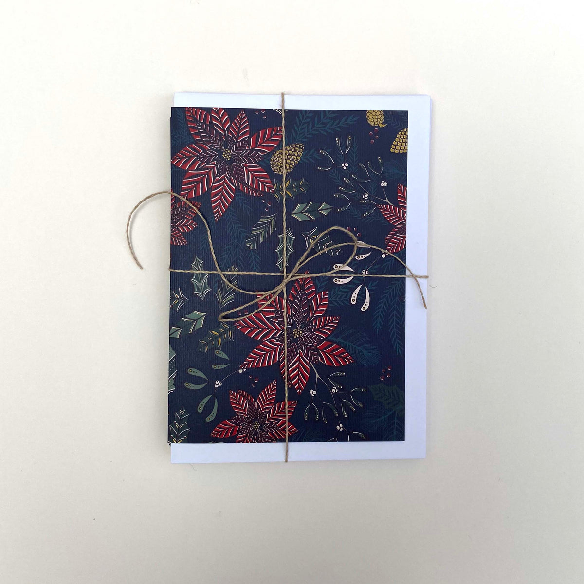 A pack of 5 rectangle Christmas greeting cards with a dark navy blue background and a festive floral pattern in red, green, and gold, wrapped with twine and presented on a light cream background.
