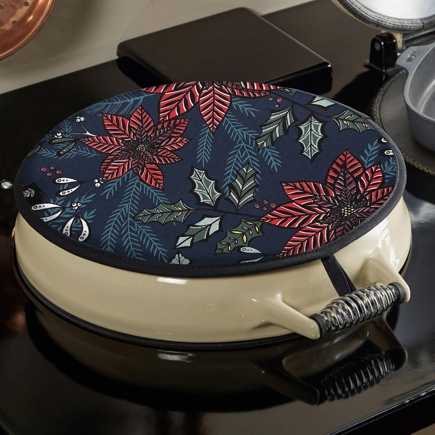 A Christmas Aga toppers has been placed on a black and cream AGA.  You can see how the hanging loop hooks onto the top of the hob.