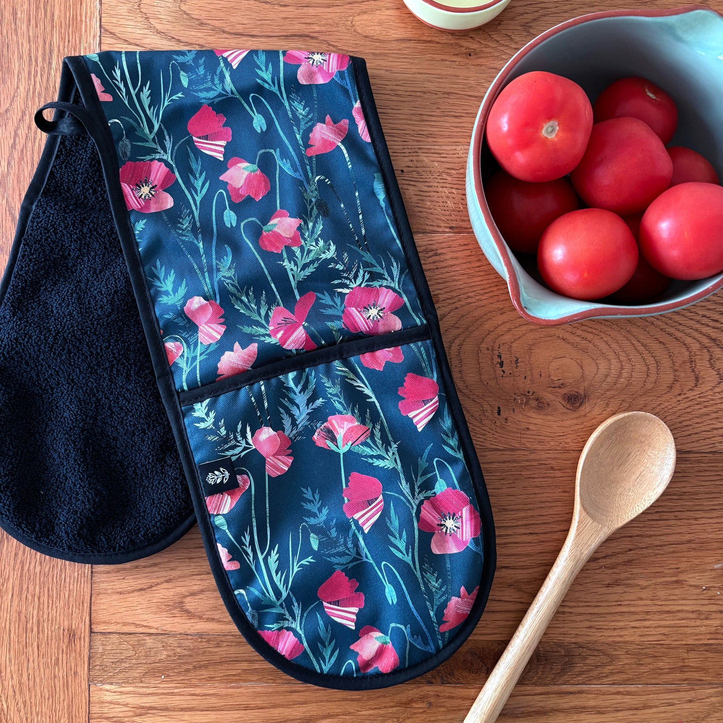 Poppy Double oven mitt on a wooden surface with a bowl of tomatoes, and a spoon.