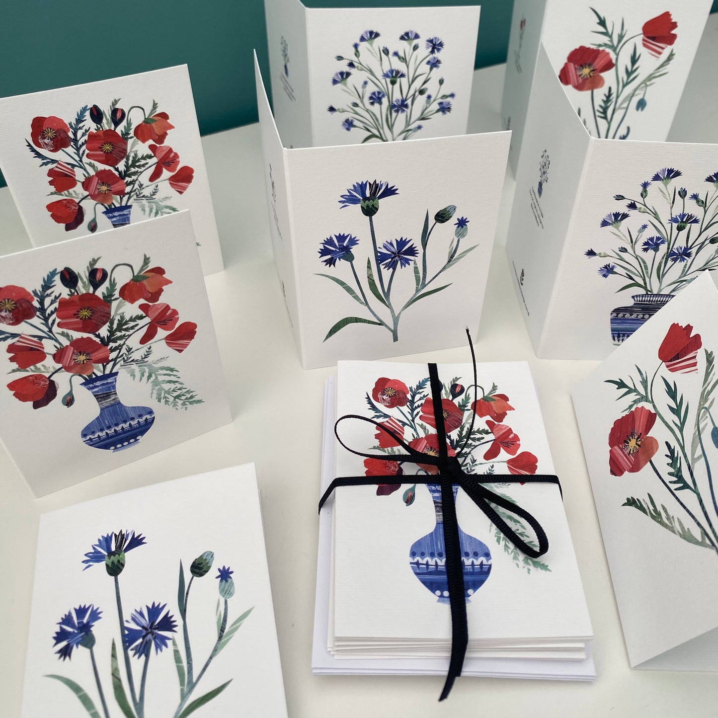 Pack of 8 mini Notecards and envelopes featuring poppies and cornflowers have been put on a white shelf. some are laying down and some are stood up open on the shelf.