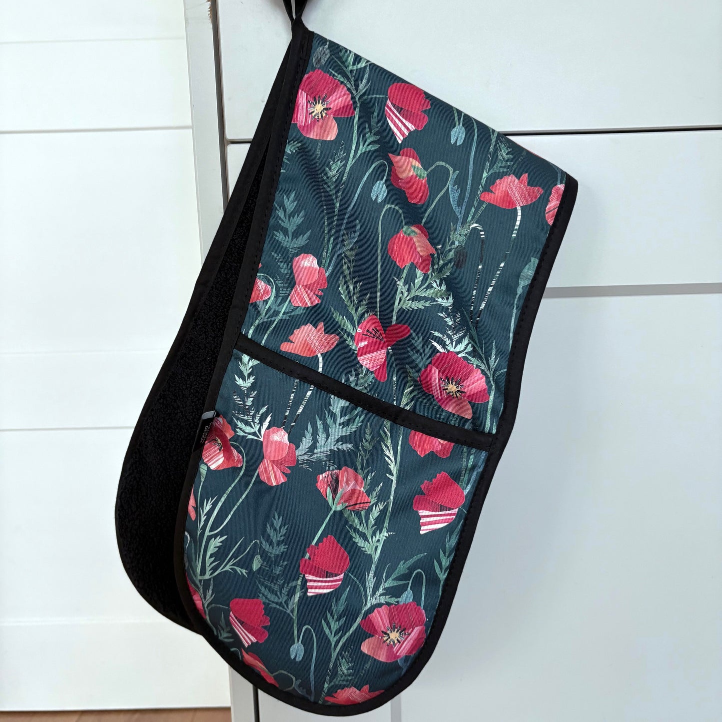 Poppy Floral-patterned oven mitt hanging on a cabinet door.
