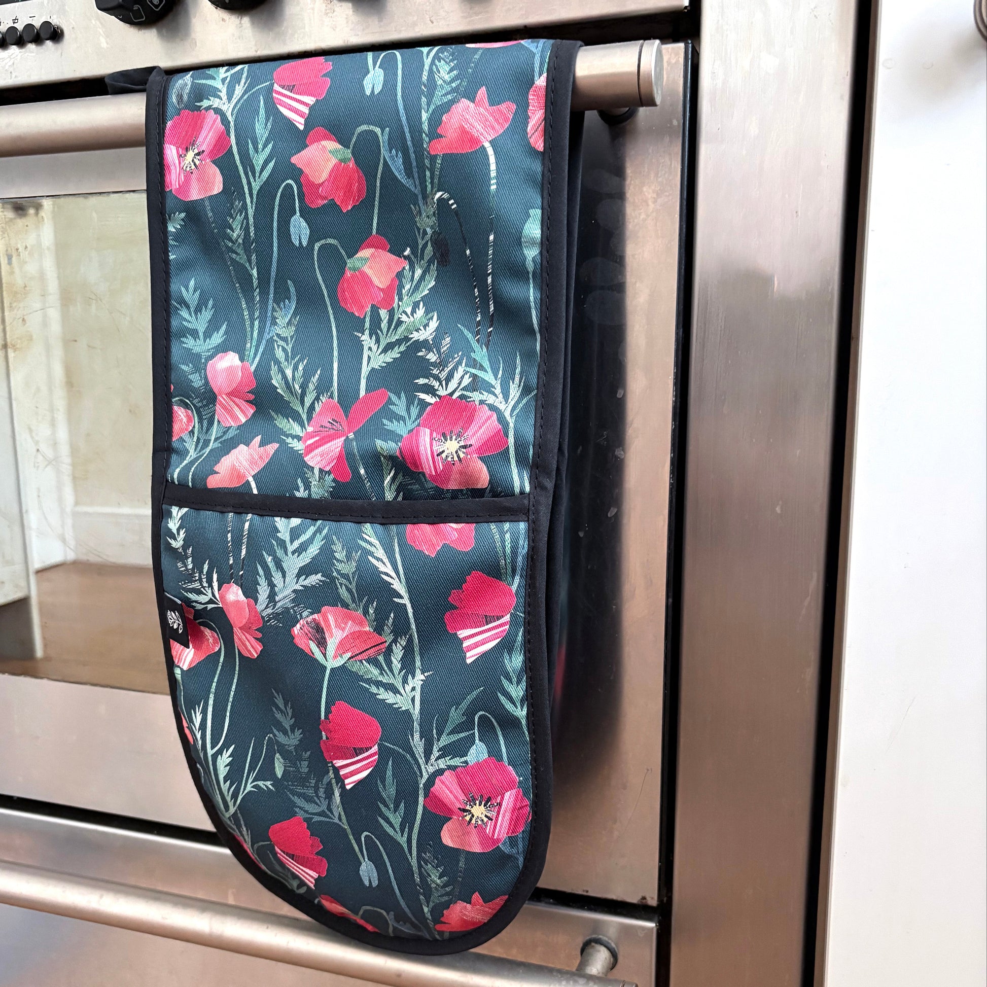 Poppy Double Oven Gloves have been hung over a rail on a stainless steel range cooker.