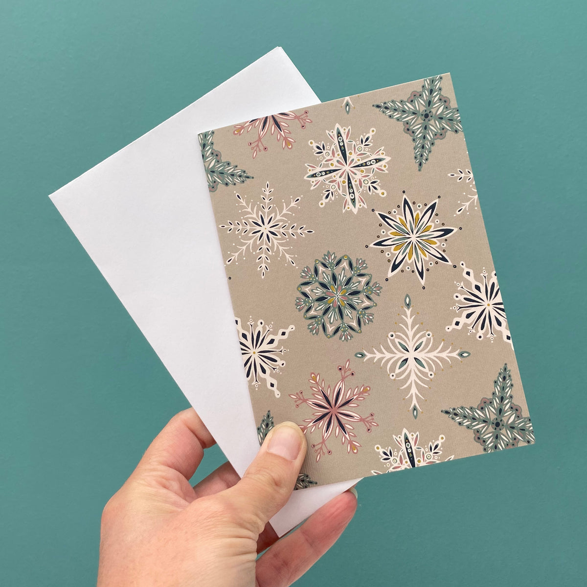 A grey Snowflake card and white envelope are being held in front of a blue green wall.