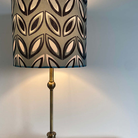 Blue Geometric Lampshade, shown here on a brass table lamp.  The design features Black and white Oval geometric shapes on a blue background.  The light is shown on in this picture.