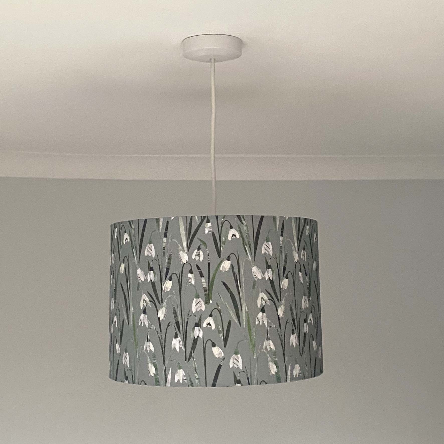 Snowdrop lampshades, shown here in a Size medium and as a Ceiling Pendant.  The design features, white and cream snowdrop flowers with different shades of green leaves printed onto a pale grey/green background.