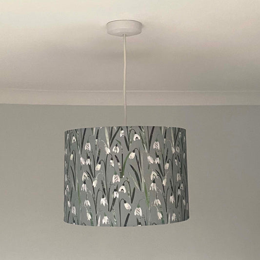 Snowdrop lampshades, shown here in a Size medium and as a Ceiling Pendant.  The design features, white and cream snowdrop flowers with different shades of green leaves printed onto a pale grey/green background.