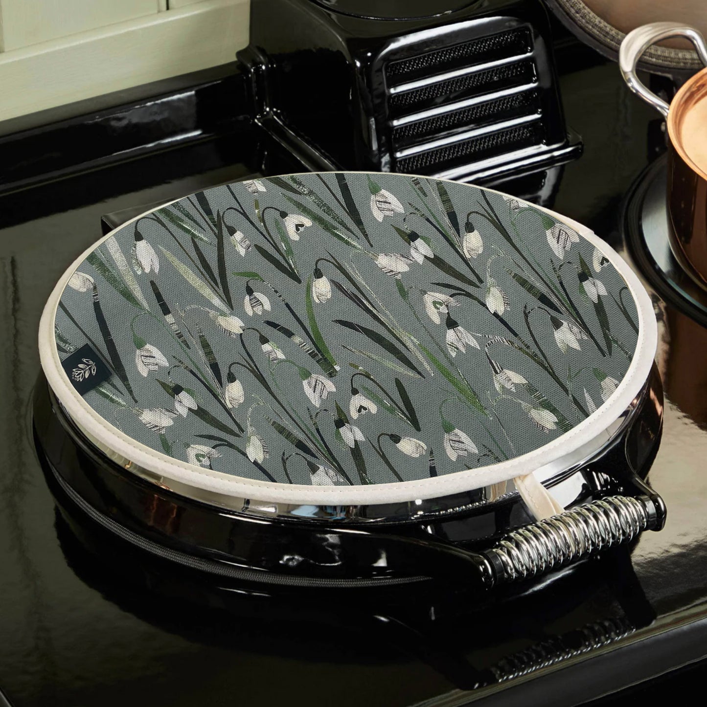 A snowdrops Aga topper has been placed on a black AGA.  You can see how the hanging loop hooks onto the top of the hob.