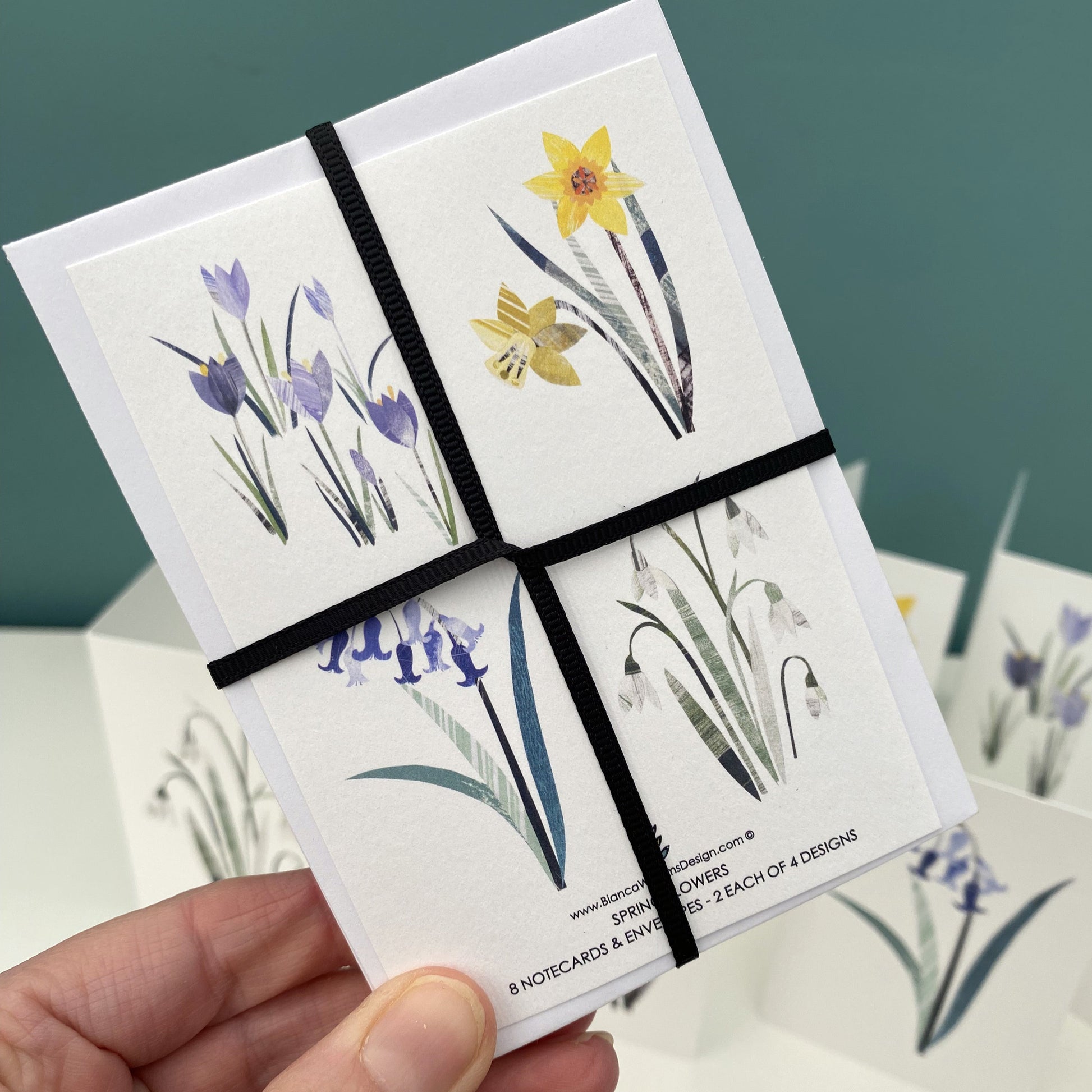 The back of a pack of floral notecards and envelopes that are being held in front of a blue green background.