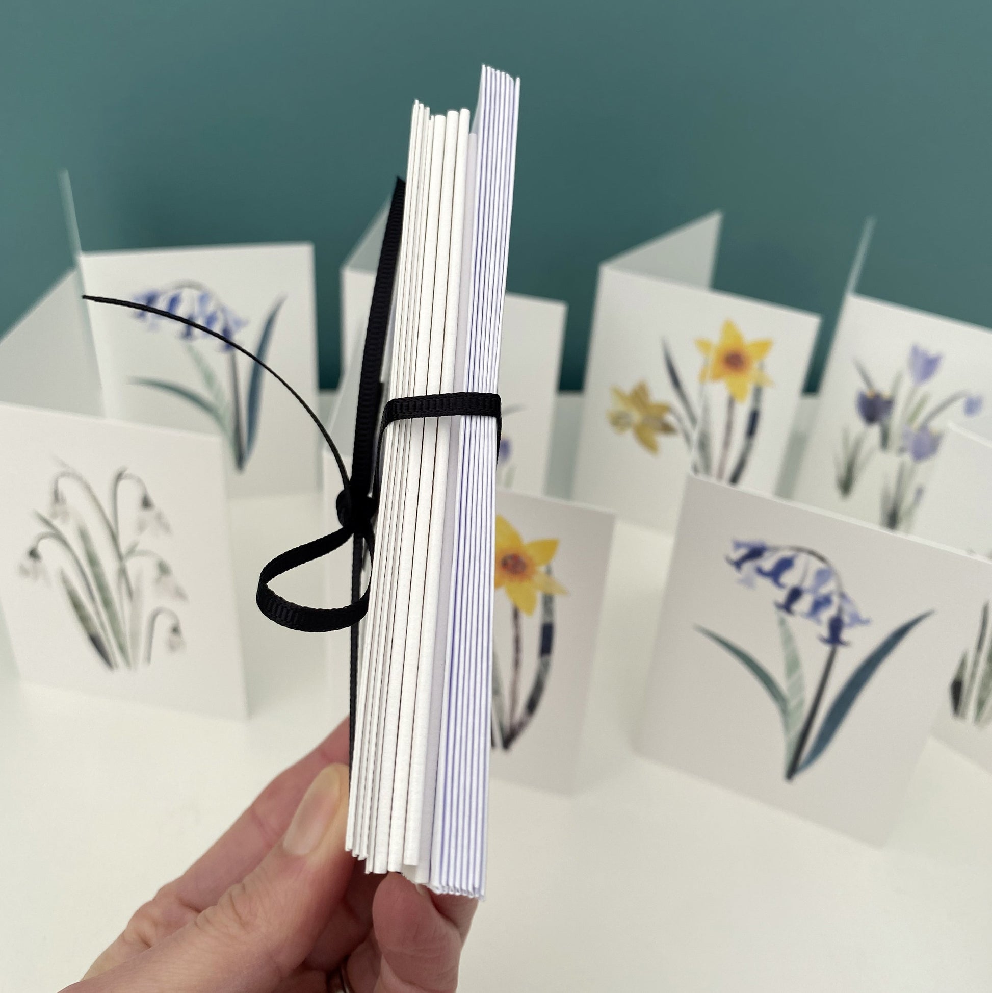 Side view of a pack of 8 notecards and envelopes tied up with black ribbon.