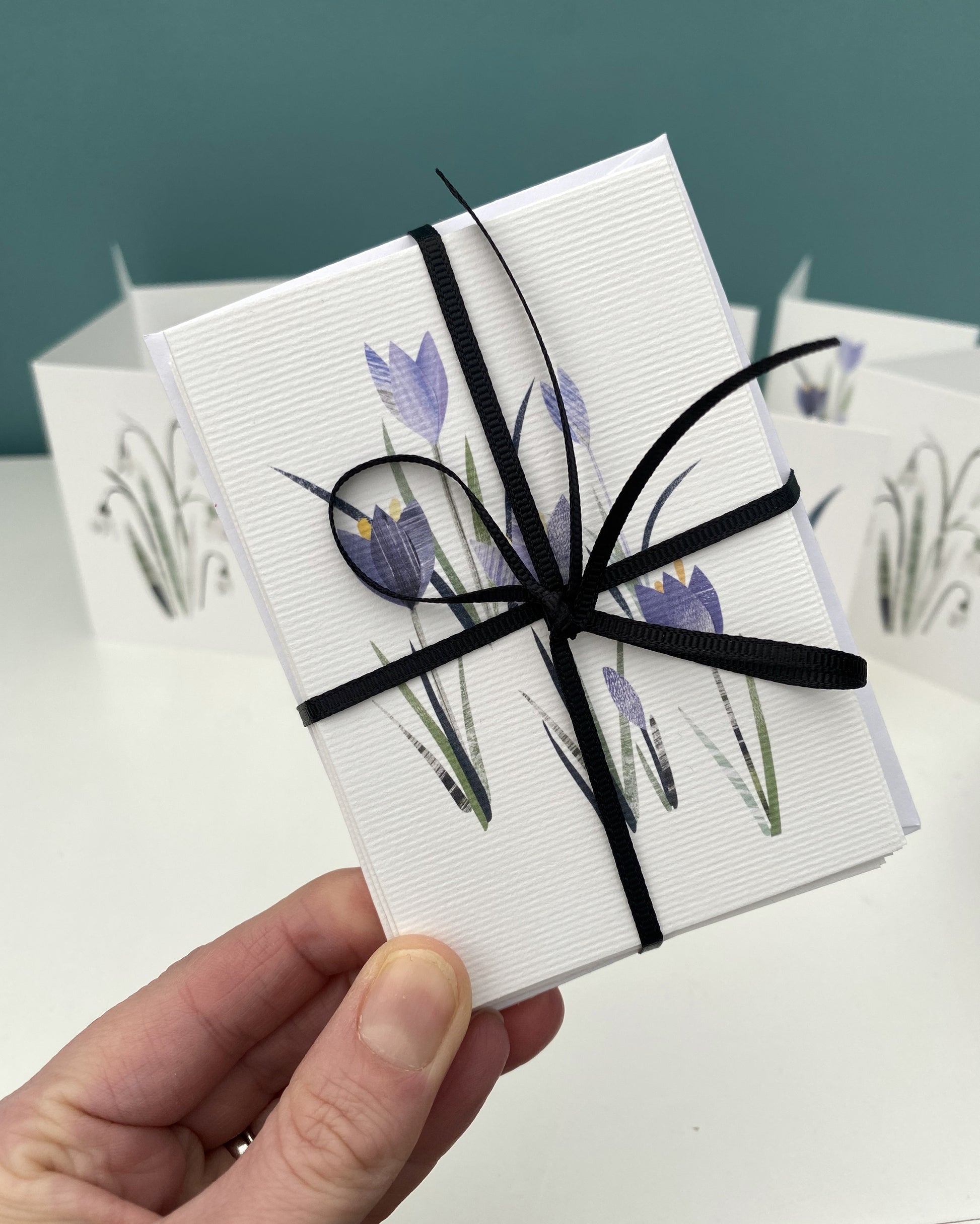 A pack of 8 mini notecards featuring Spring Flowers have been tied up with black ribbon and are being held.