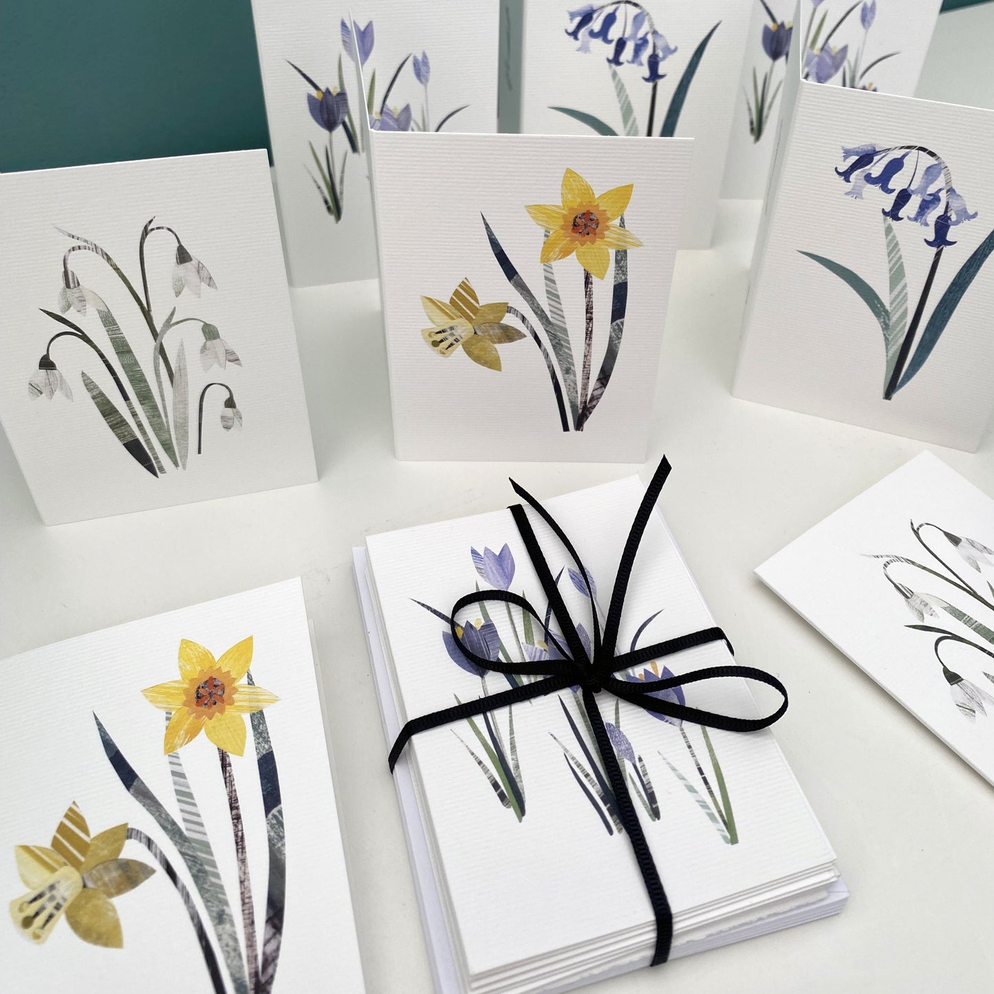 Pack of 8 mini Notecards and envelopes featuring spring flowers.  They have been put on a white shelf. some are laying down and some are stood up open on the shelf.