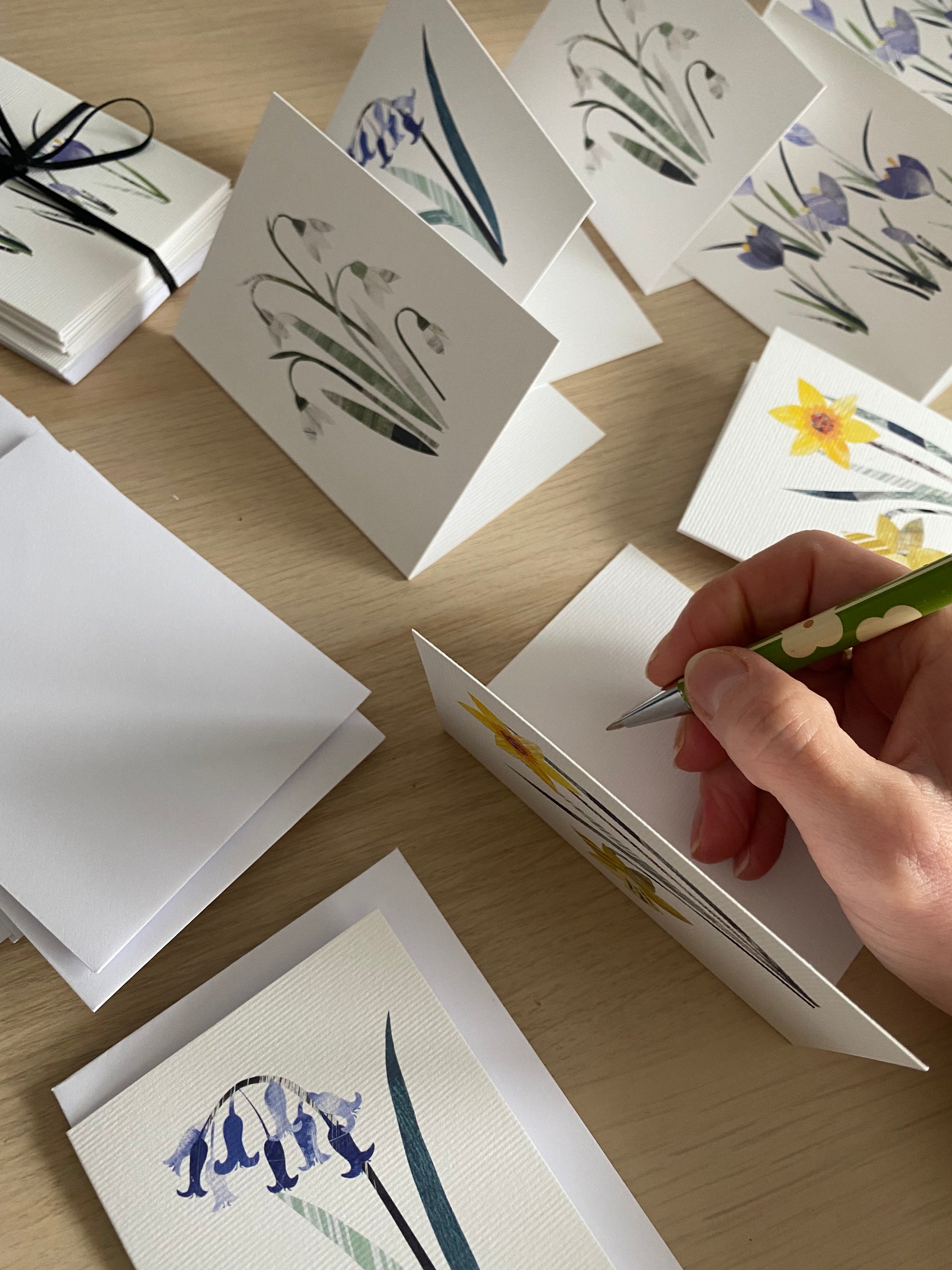 The easter floral notecards have been opened and placed on a wooden table.  One card is about to be written in.