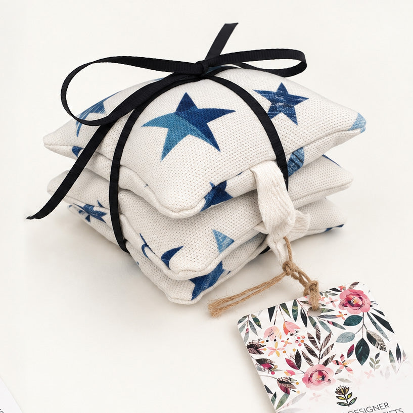 Three small square fabric pouches tied together with a black ribbon bow, decorated with blue star patterns on a white woven background. A floral paper tag hangs from the tassel, and the product is photographed on a clean white surface.
