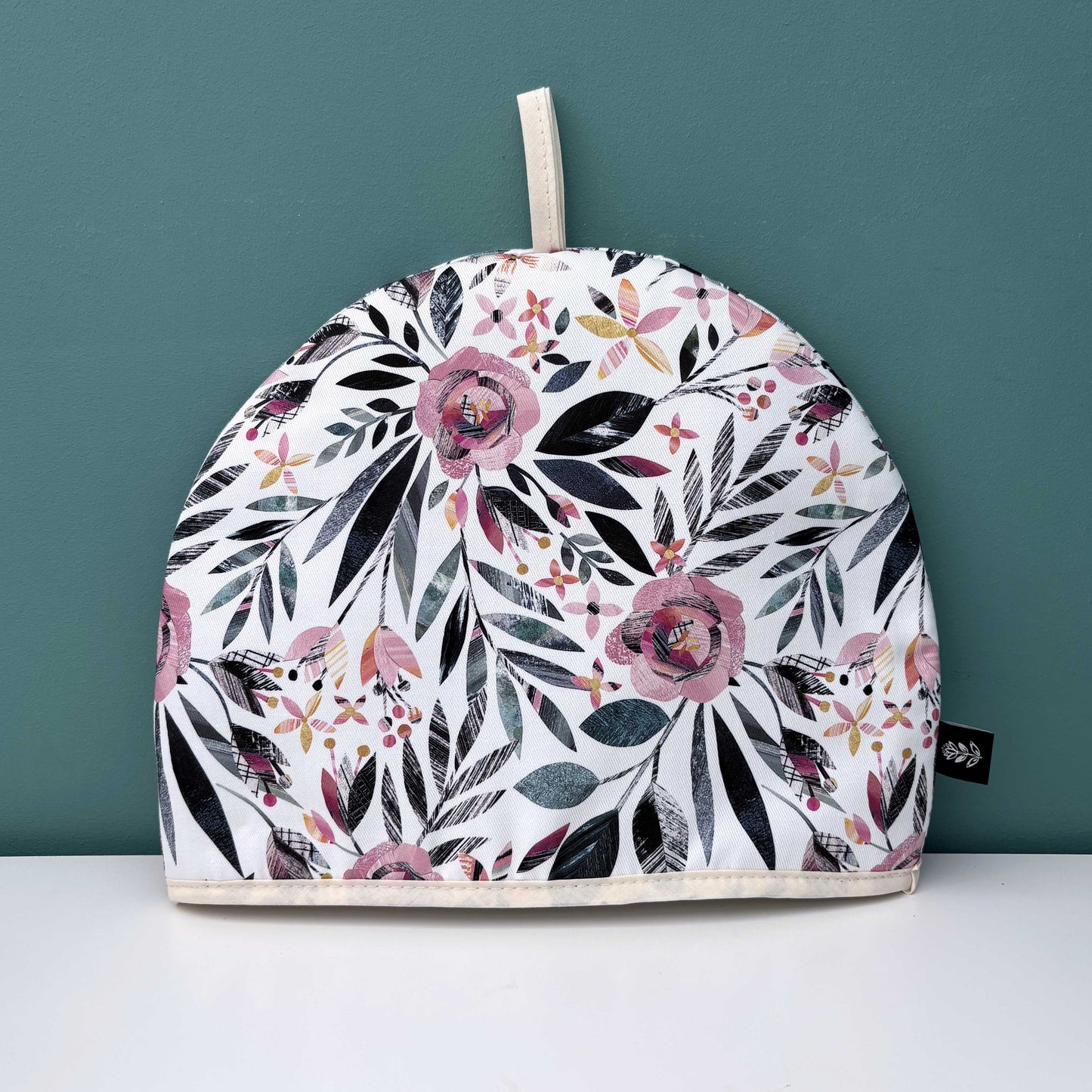 A Summer Floral patterned tea cosy on a white surface with a teal background.