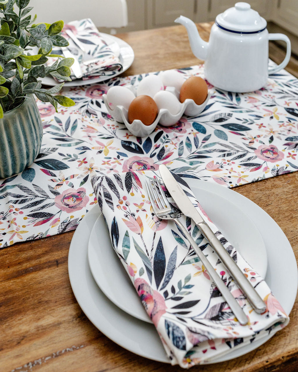 Dining table setting with Summer Floral table runner and matching napkins, plates, and cutlery on a wooden table.