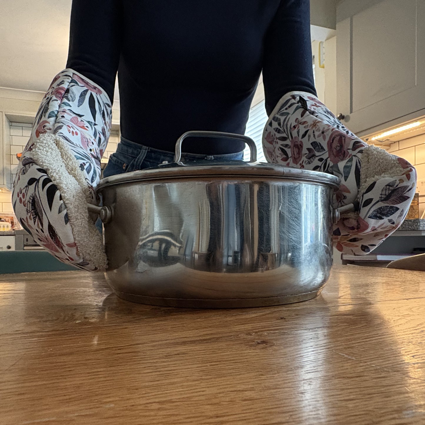 The Summer Floral single oven mitts are being worn to carry a hot sauce pan out of the oven and on to a wooden table.