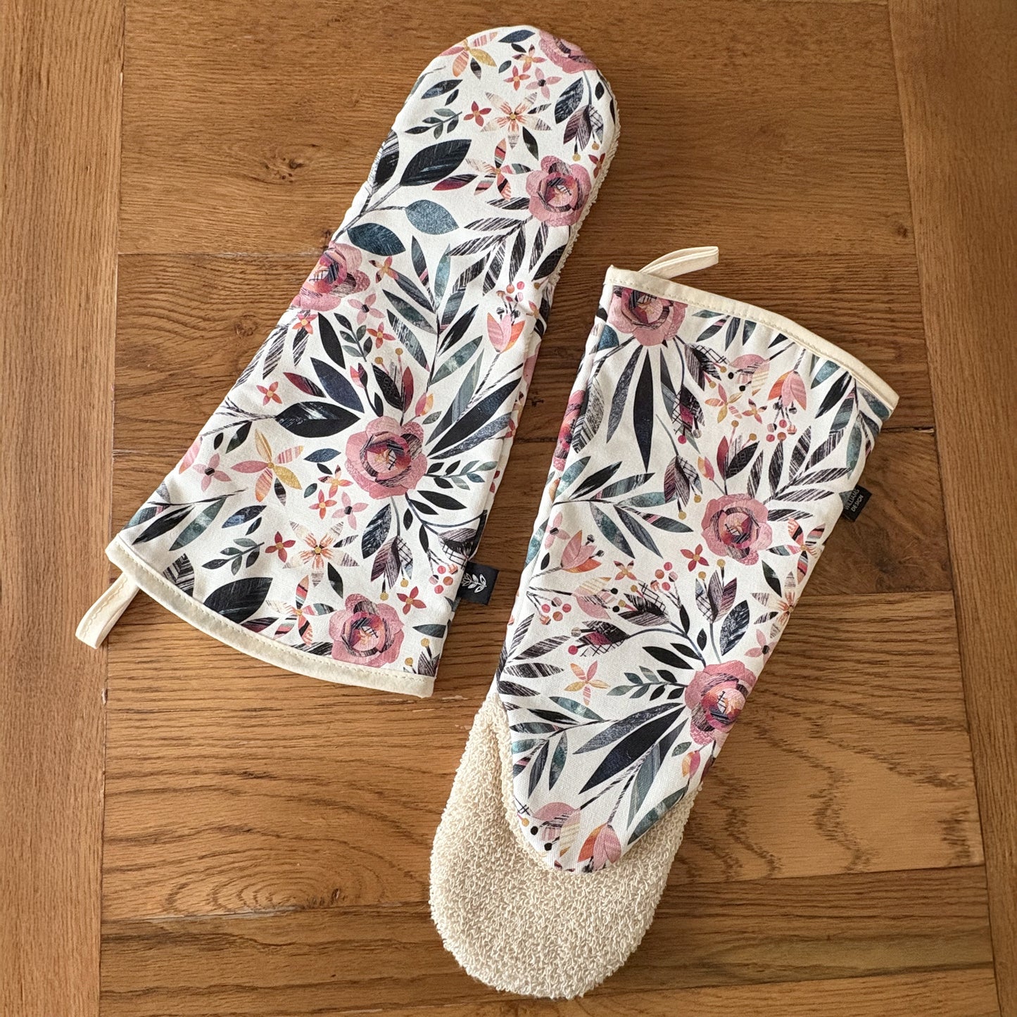 Two Summer Floral Gauntlet style Oven mitts have been placed on a wooden table.  One placed on the front than one shows the back.