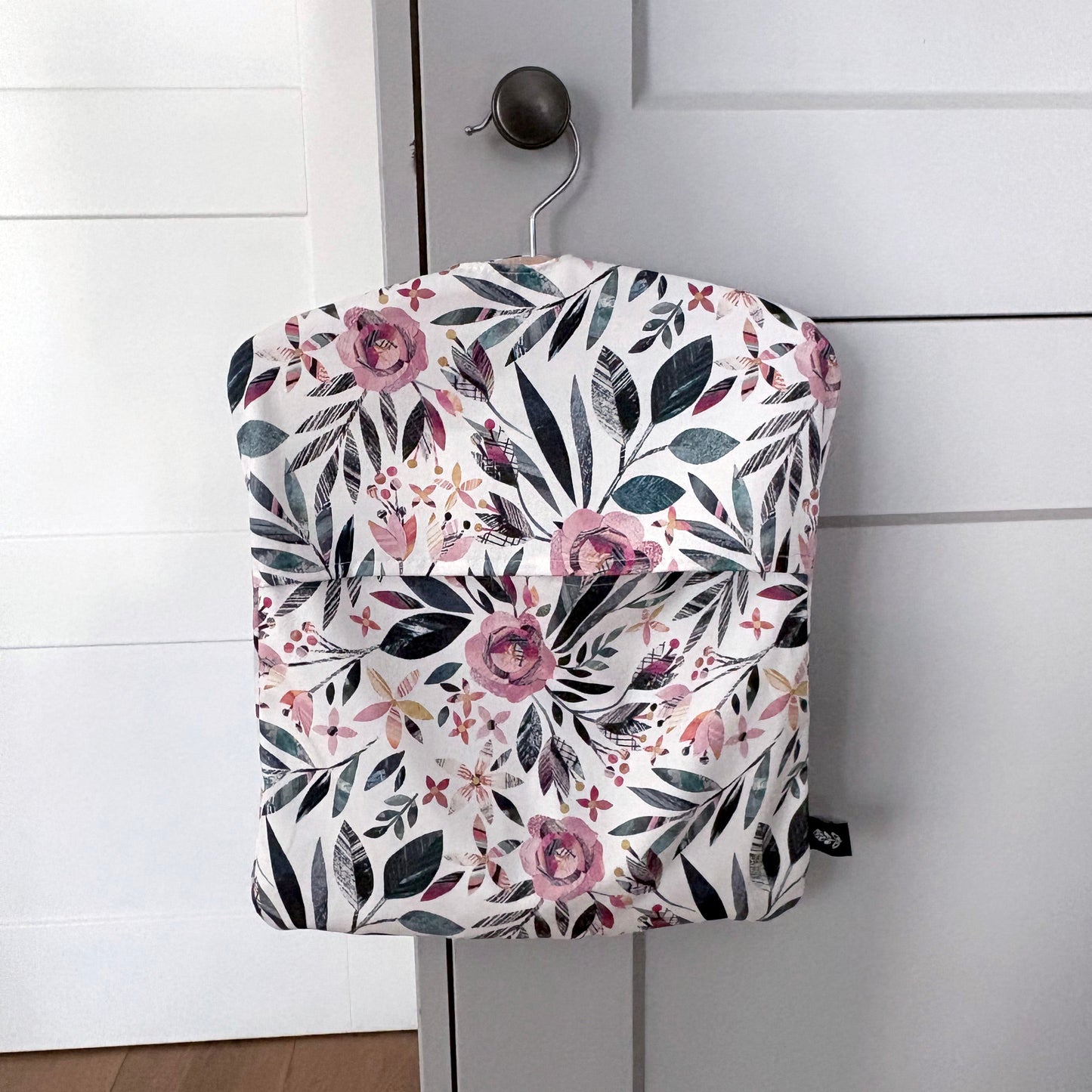 A Summer Floral peg bag featuring a pink and green pattern has been hung on a pale grey kitchen door knob.