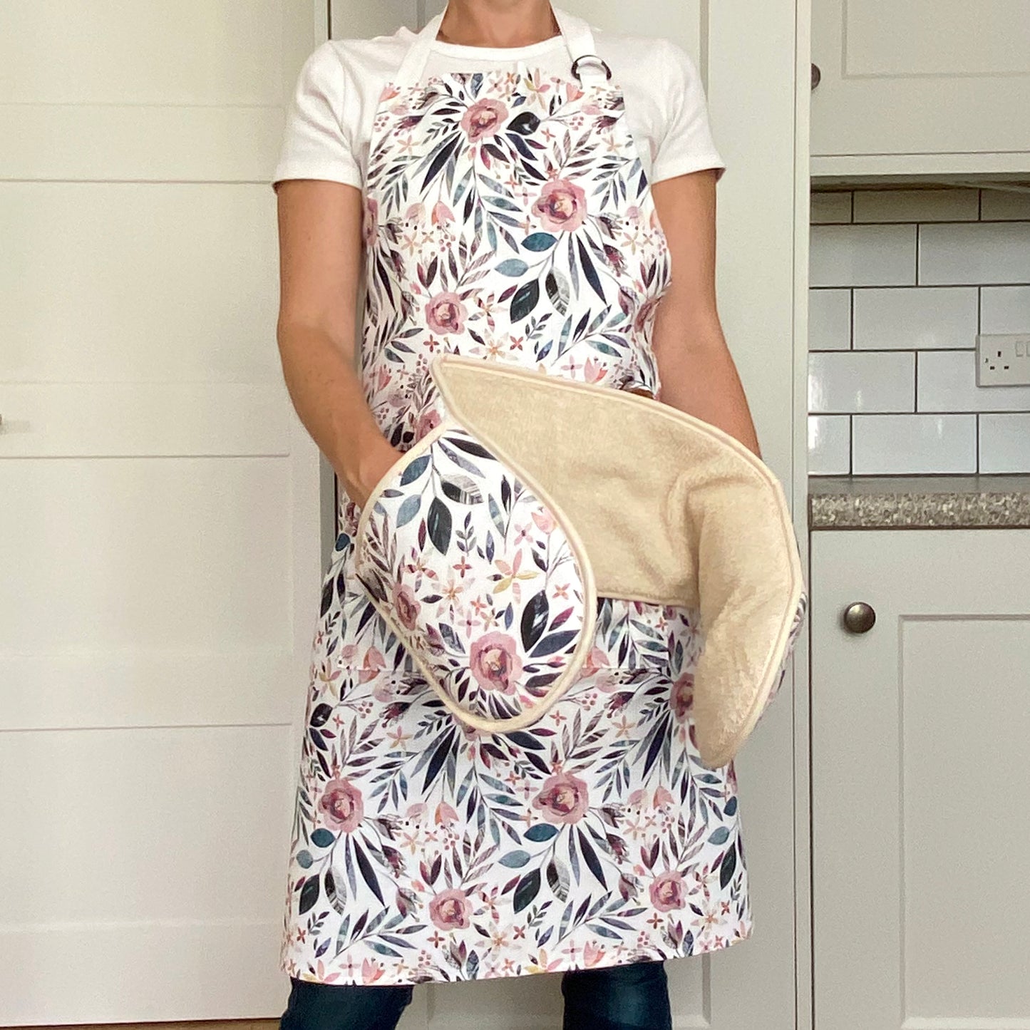 Model wears a pink and green summer floral apron, she also has a pain of matching double Oven Gloves on her hands.