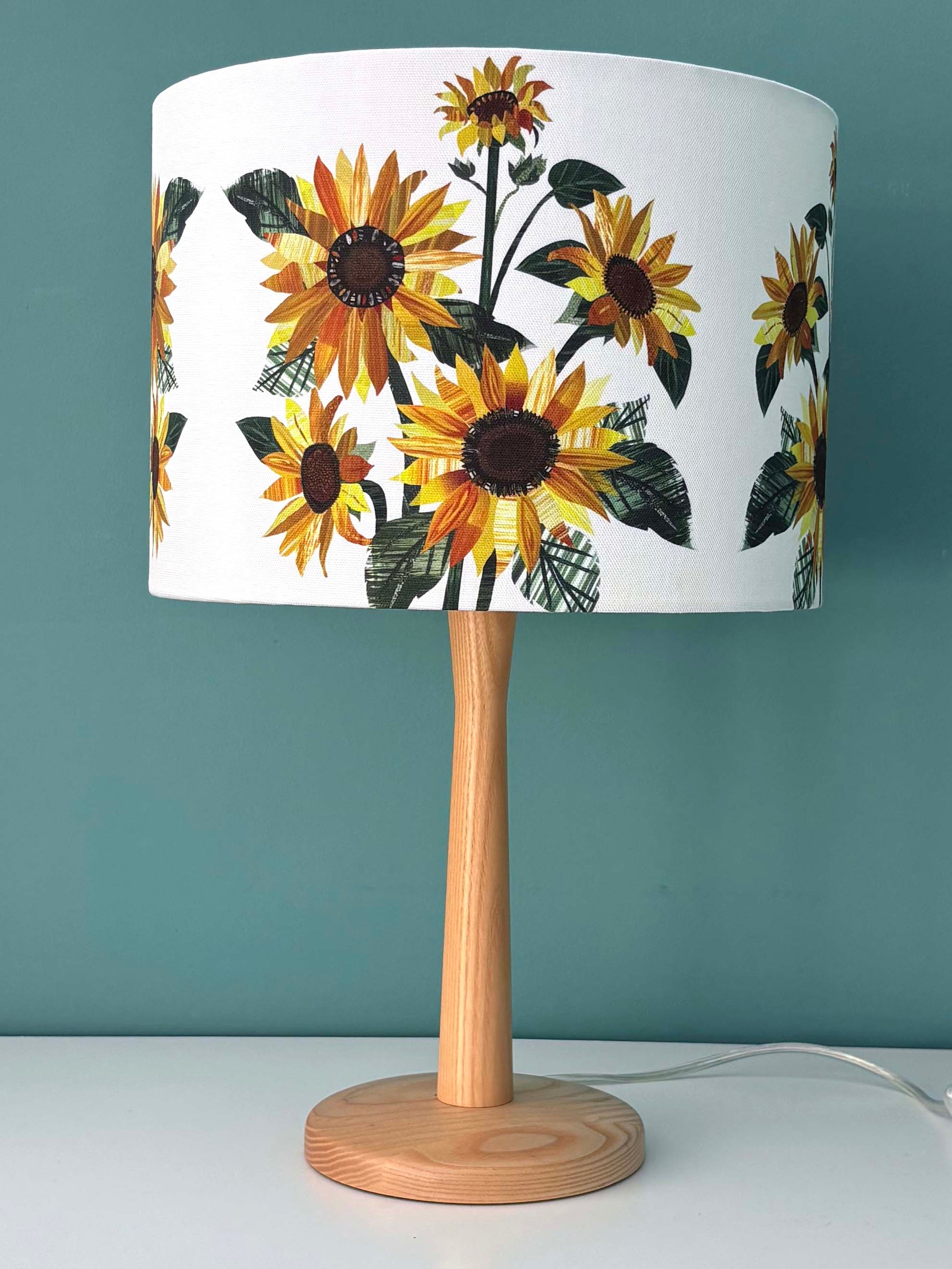 A 30cm Table lamp with sunflower patterned shade against a blue green wall.