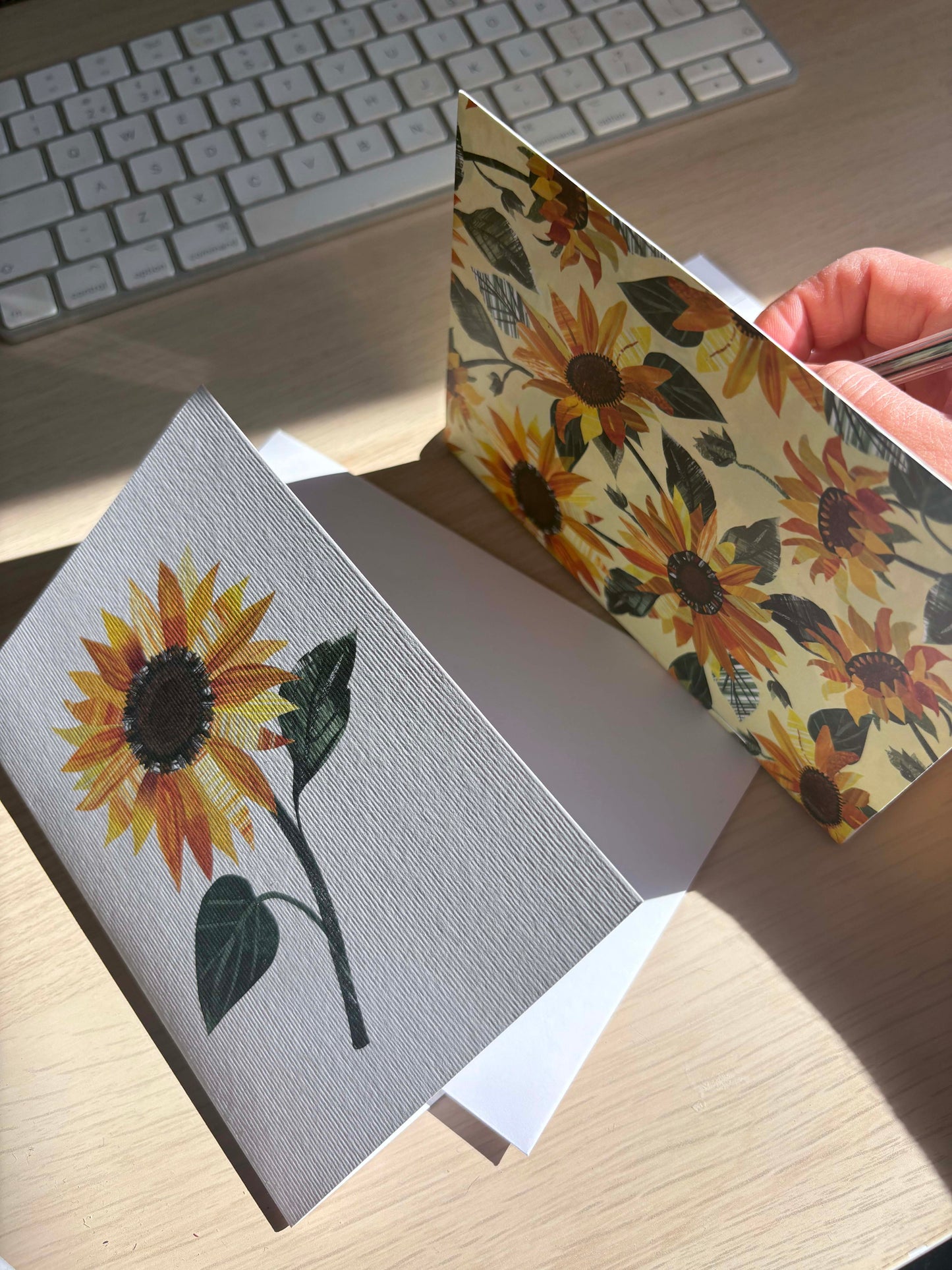 A yellow Sunflower Notebook is being written in on a wooden desk.  A matching Sunflower card can be seen beside the Notebook.