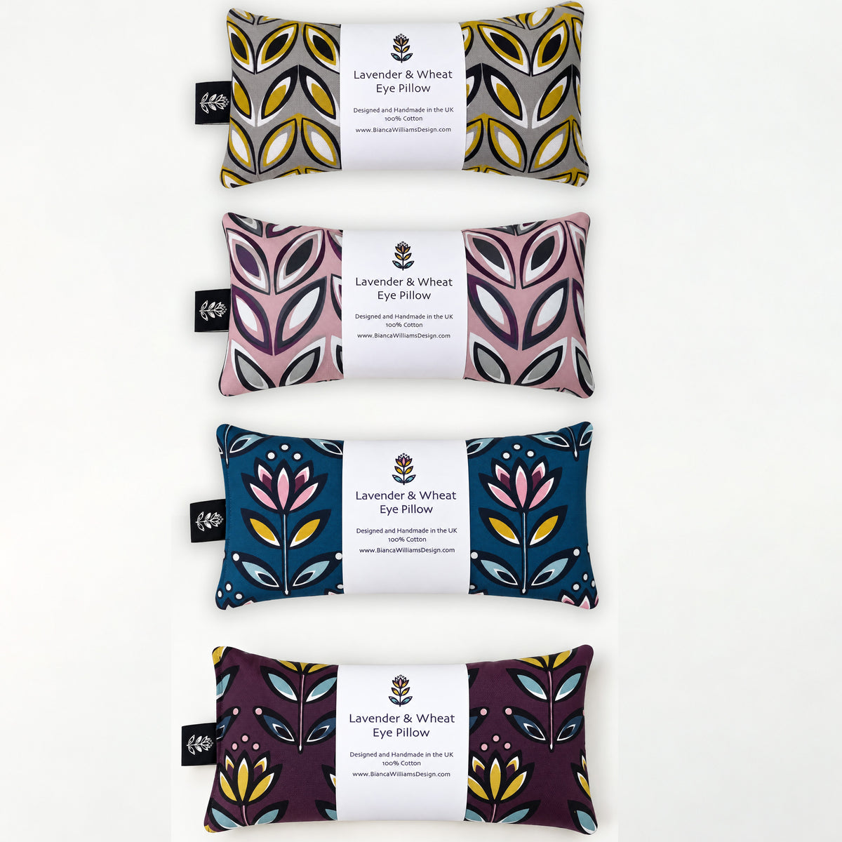 Four rectangular eye pillows arranged vertically on a white background, each with a white paper label reading 'Lavender & Wheat Eye Pillow' and a small black fabric tag. The pillows feature different floral and geometric textile patterns in lavender, yellow, gray, pink, blue, and purple tones.
