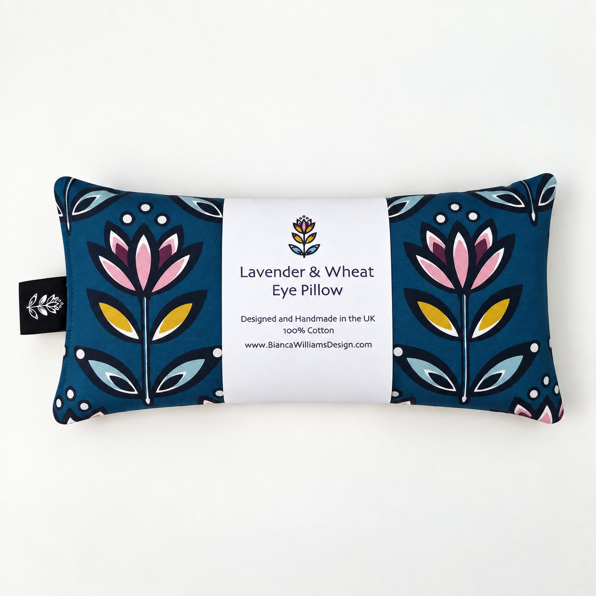 A rectangular lavender and wheat eye pillow by Bianca Williams Design, featuring a Teak background with a stylised floral pattern in pink, yellow, and light blue, wrapped in a white paper band with product details.