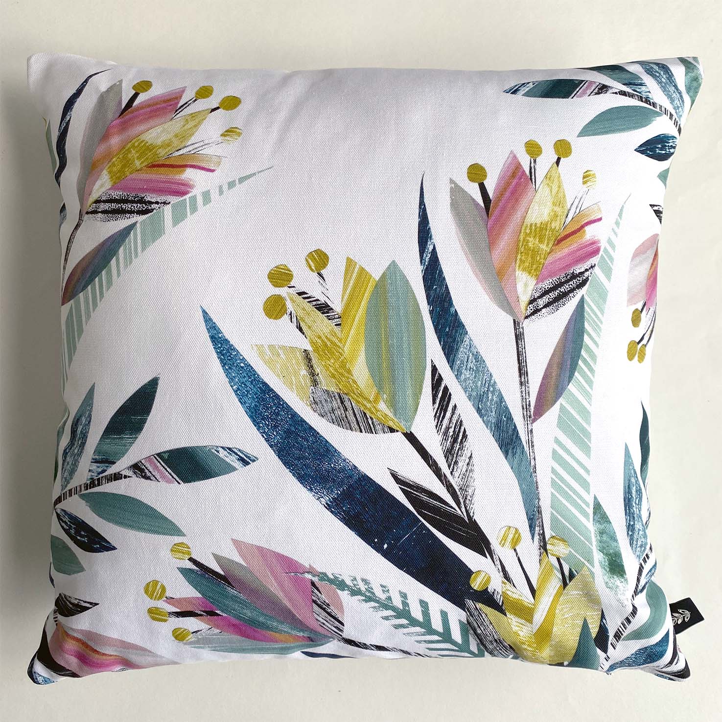  A square Tulip Cushion featuring textured Pink and Yellow Tulips with green leaves in a placement print on a plain white Cushion.  It has been placed on a white background.