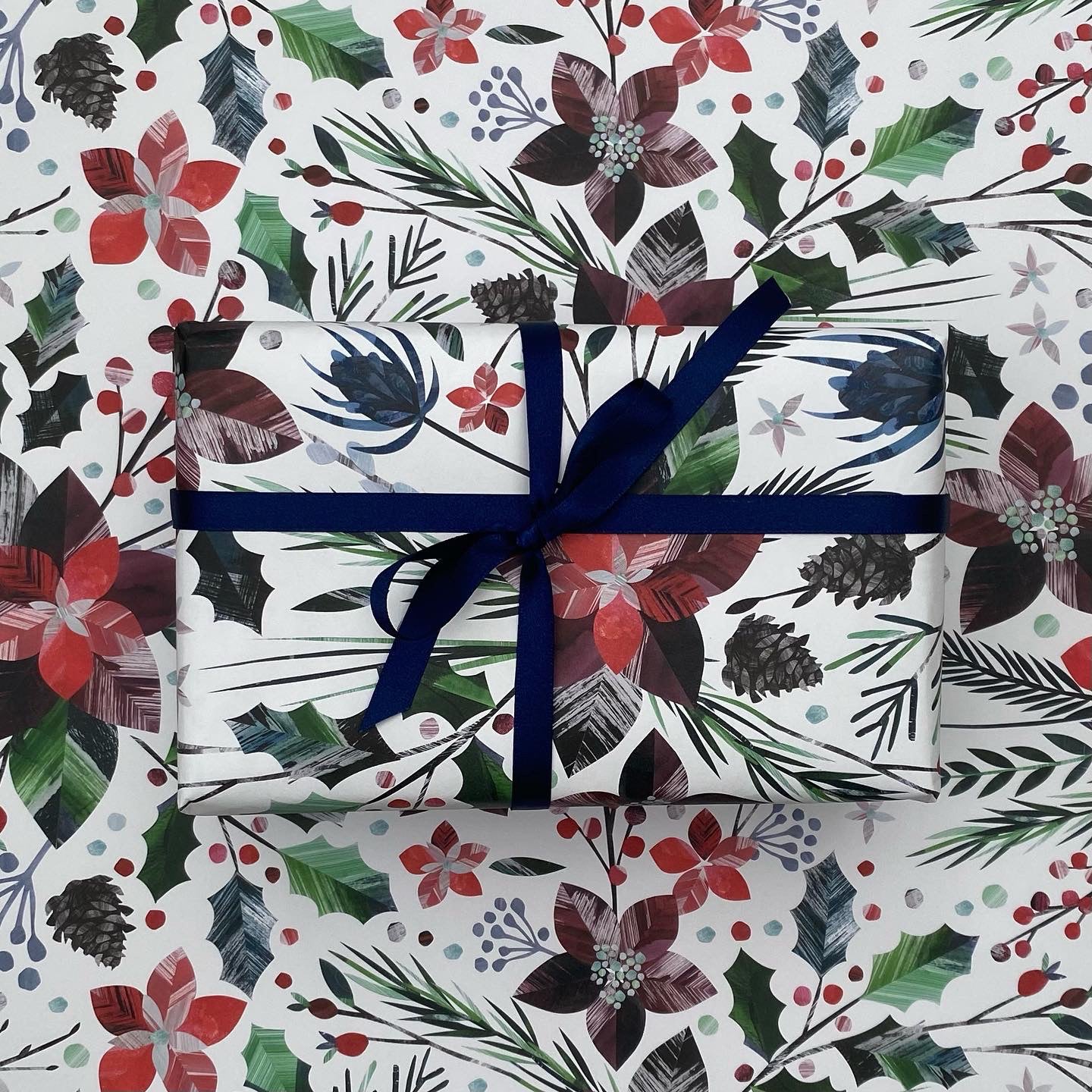 A present has been wrapped in the winter Floral Christmas wrapping paper and has been tied with dark blue satin ribbon in a bow. The present has been placed on a sheet of the winter floral gift wrap.