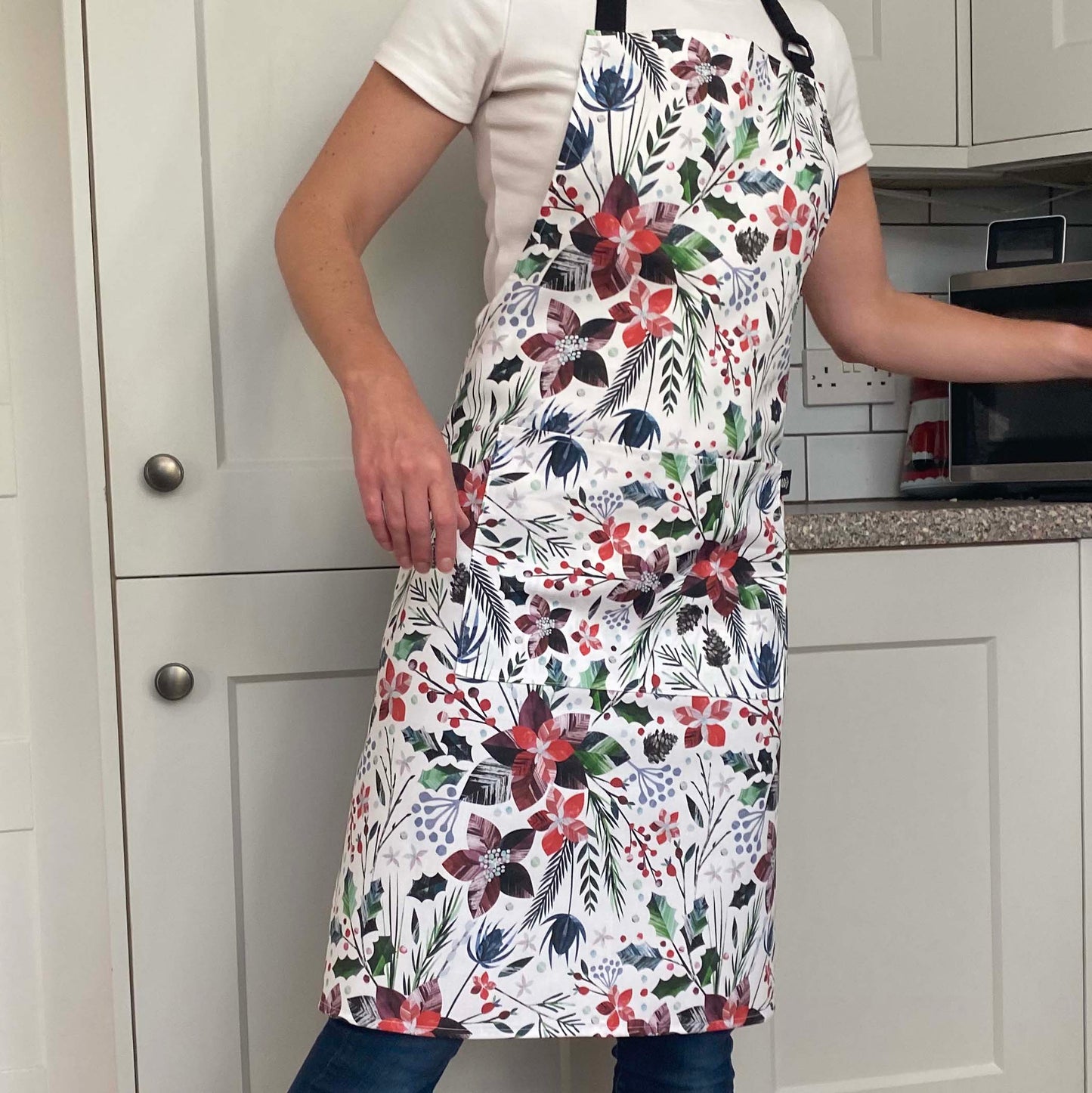 A model is wearing the Winter Floral Apron which features red Poinsettia Flowers with green sprigs and red berries.