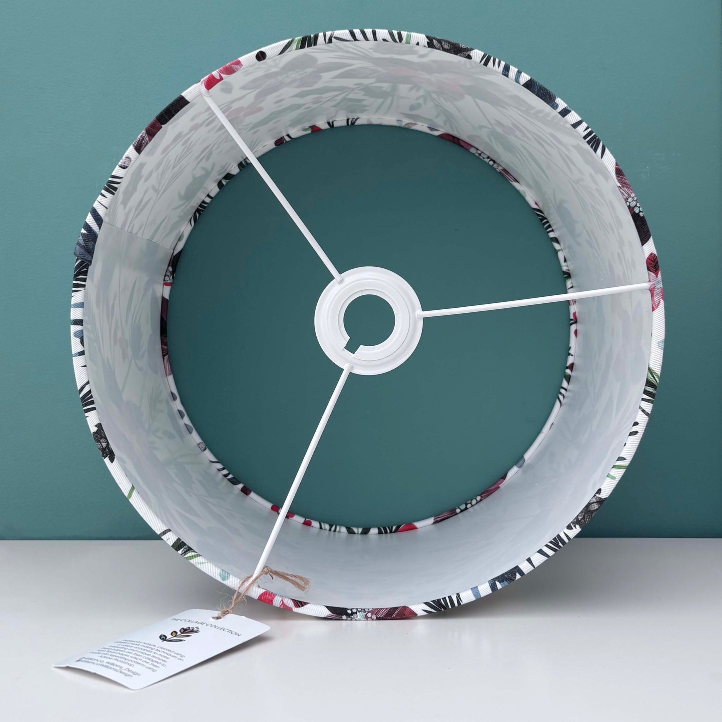 Inside a Winter Floral patterned lampshade.  It has been placed on a white shelf against a blue green background.