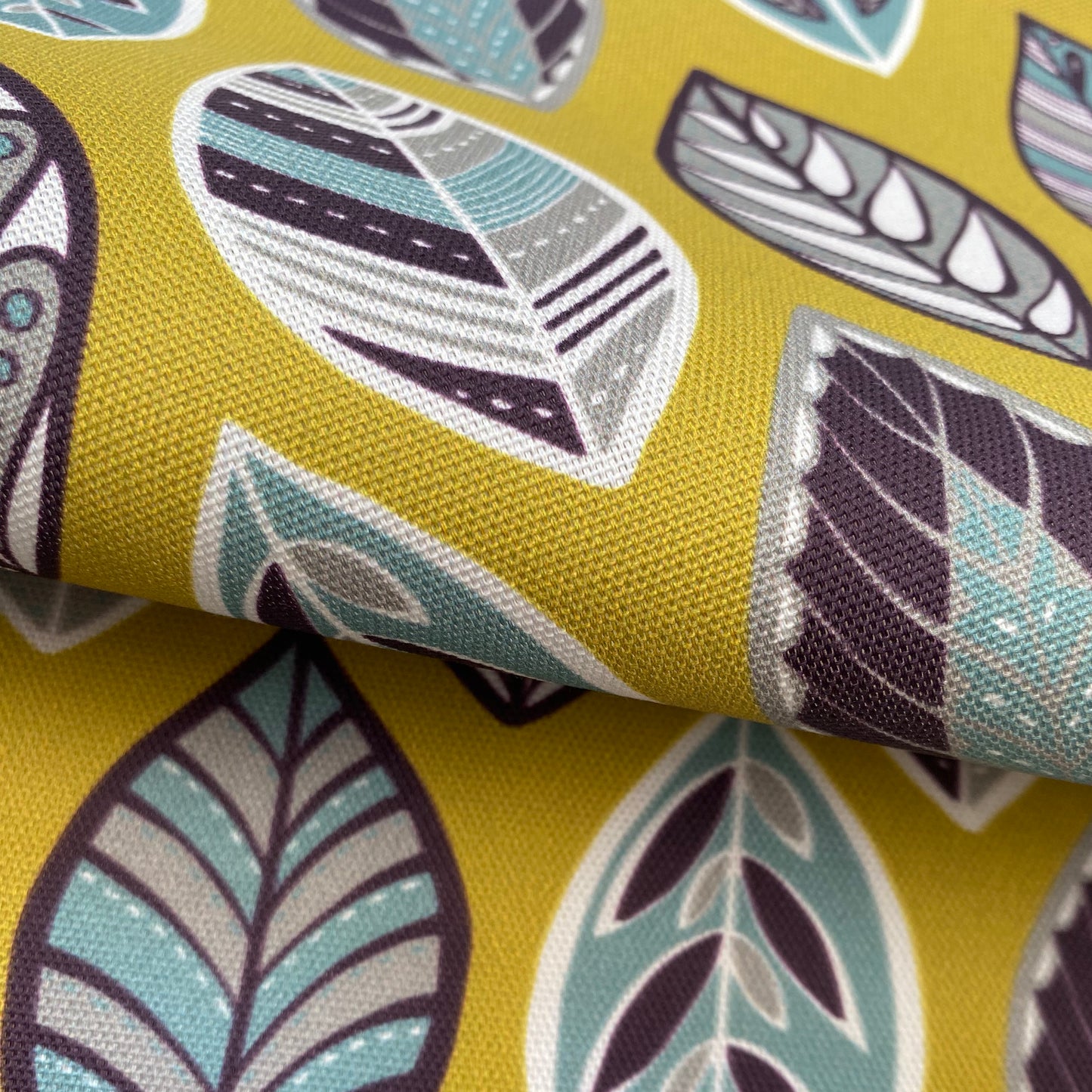 Close up of the Yellow Beech Leaf fabric featuring simple leaf motifs in white, blue, aubergine and grey on a yellow background.