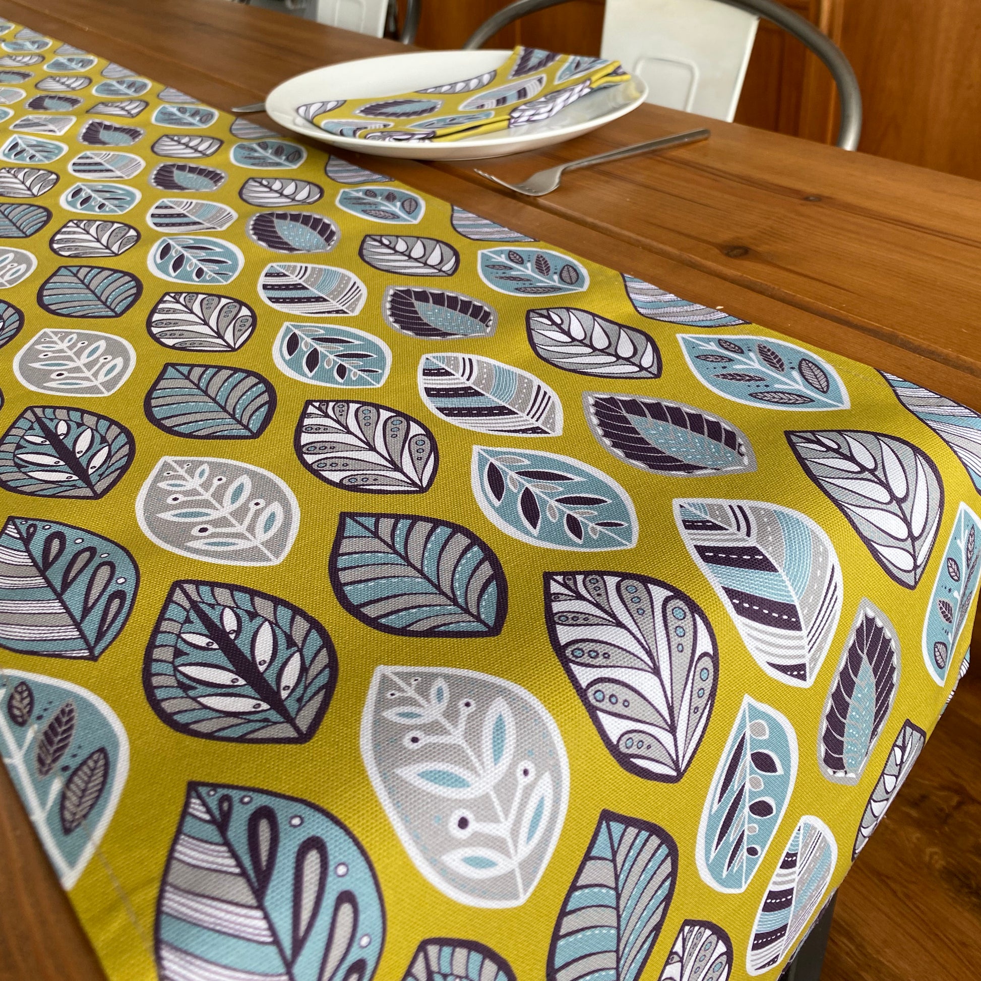 Close up of the yellow beech leaf table runner.  It features a simple hand drawn leaf motif in white, grey, blue and aubergine printed onto a yellow background.