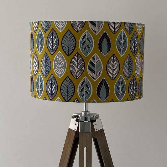 Large Yellow Beech Leaf Lampshade.  Displayed here on a wooden tripod floor lamp.  The design features a leaf motif in a Skandinavian style featuring Blue, grey and white leaf shapes on a yellow background.