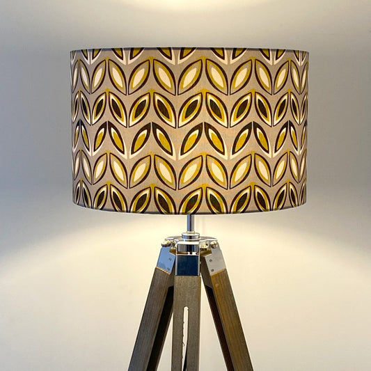 Yellow and Grey Geo pattern, on a large lampshade on wooden tripod floor lamp.  The pattern features black, yellow and off white oval shapes on a mid grey background.  The light is on in this picture.