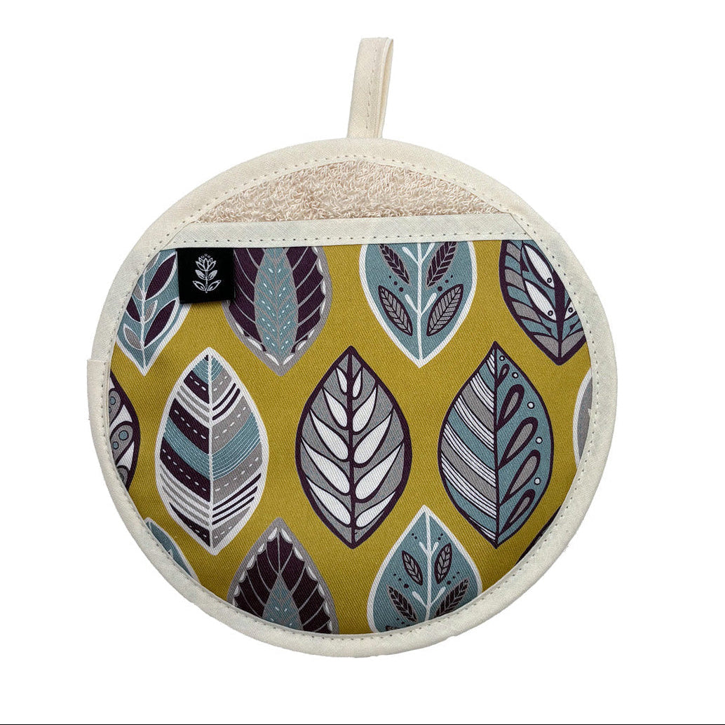A round fabric pot holder with a mustard yellow background and a pattern of stylized leaves in teal, purple, gray, and white. It features a cream-colored stitched border and a matching fabric loop at the top.