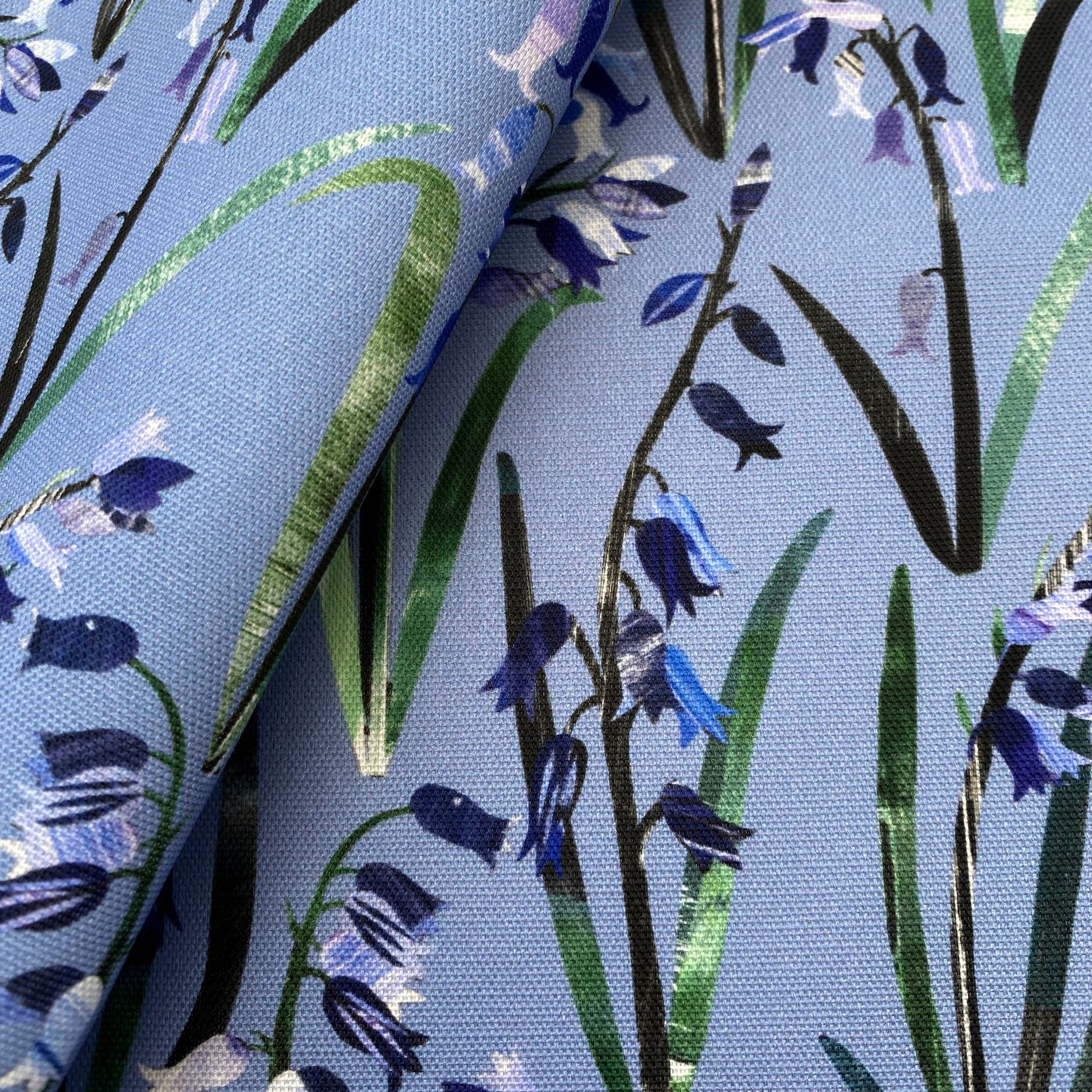 Close up of textured Bluebells with green leaves printed onto a Blue cotton background.