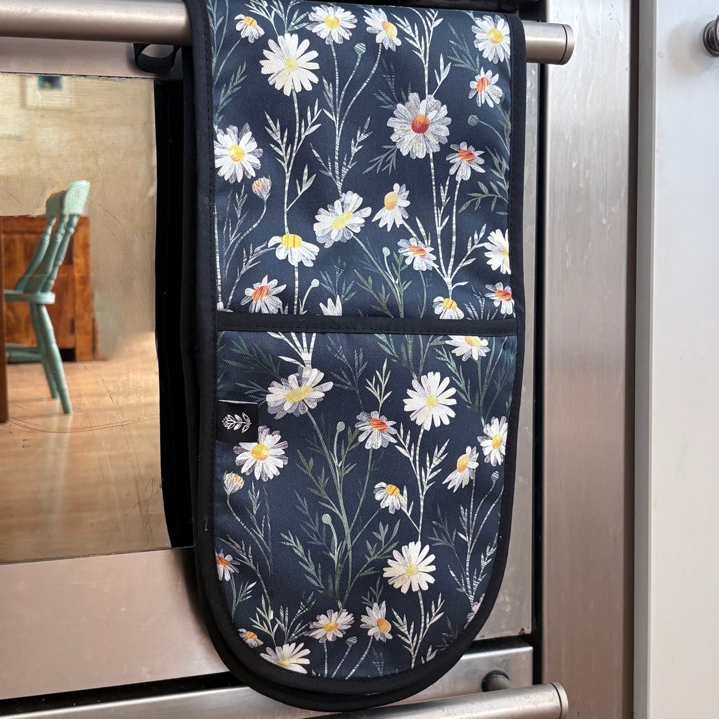 Daisy Floral-patterned oven mitt hanging on a stove handle.