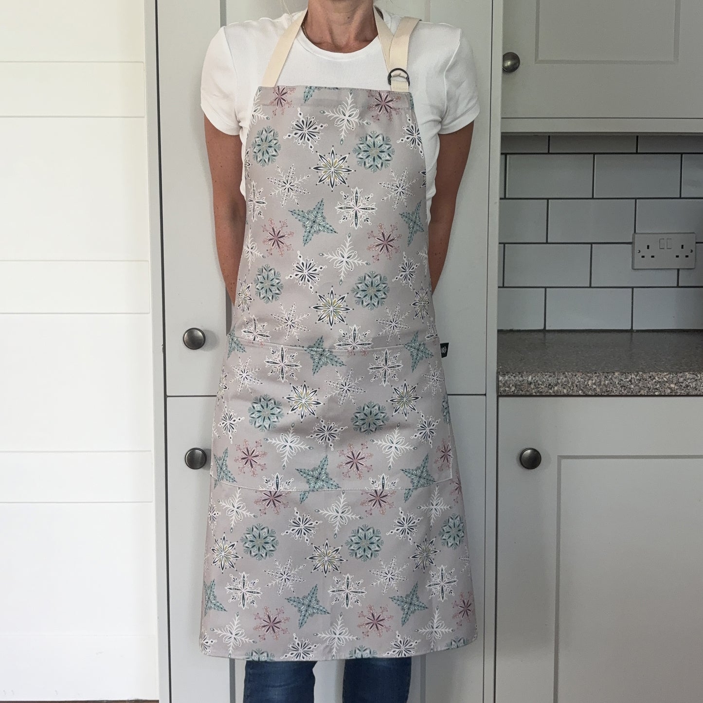 A person wearing a grey snowflake apron in a grey kitchen.