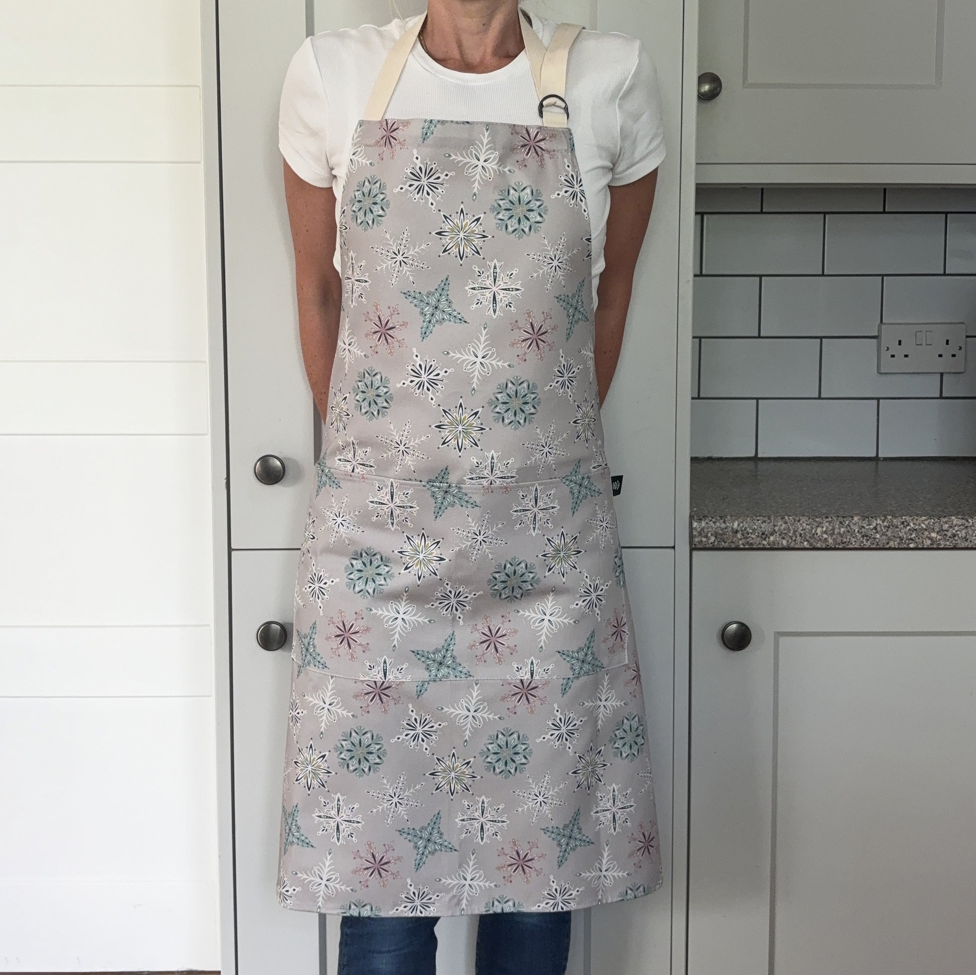 A person wearing a grey snowflake apron in a grey kitchen.